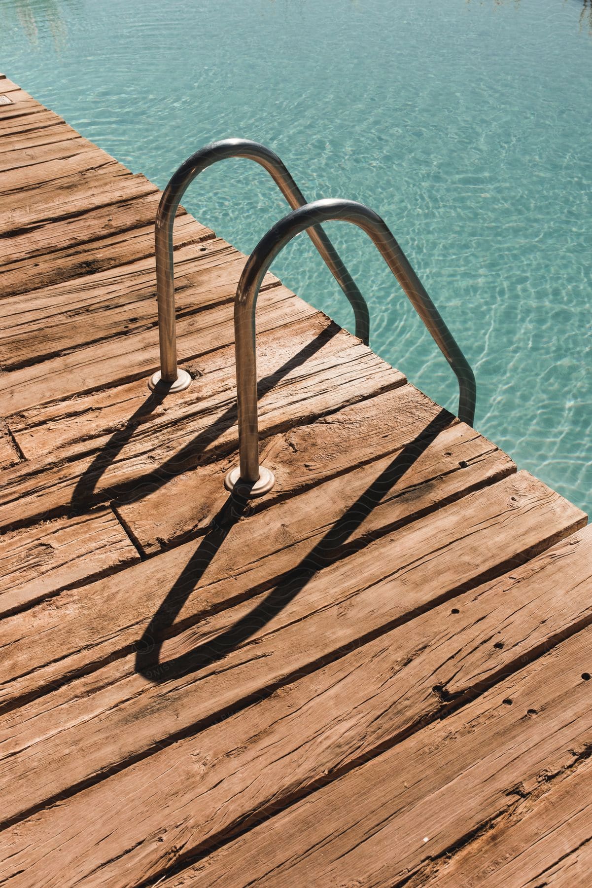 A wooden dock with a metal railing leading into a pool on a hot summer day