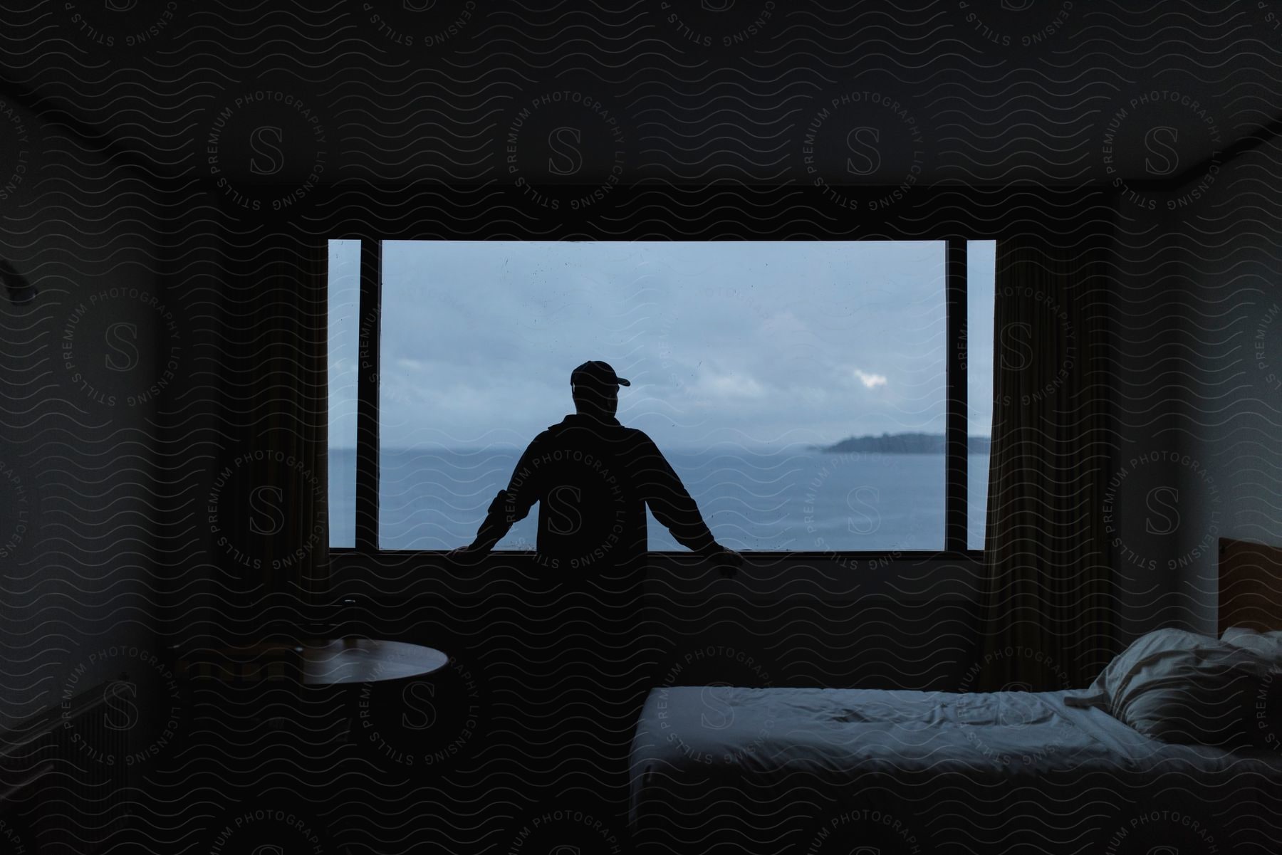 A man looks out a window at the ocean with the coast in the distance