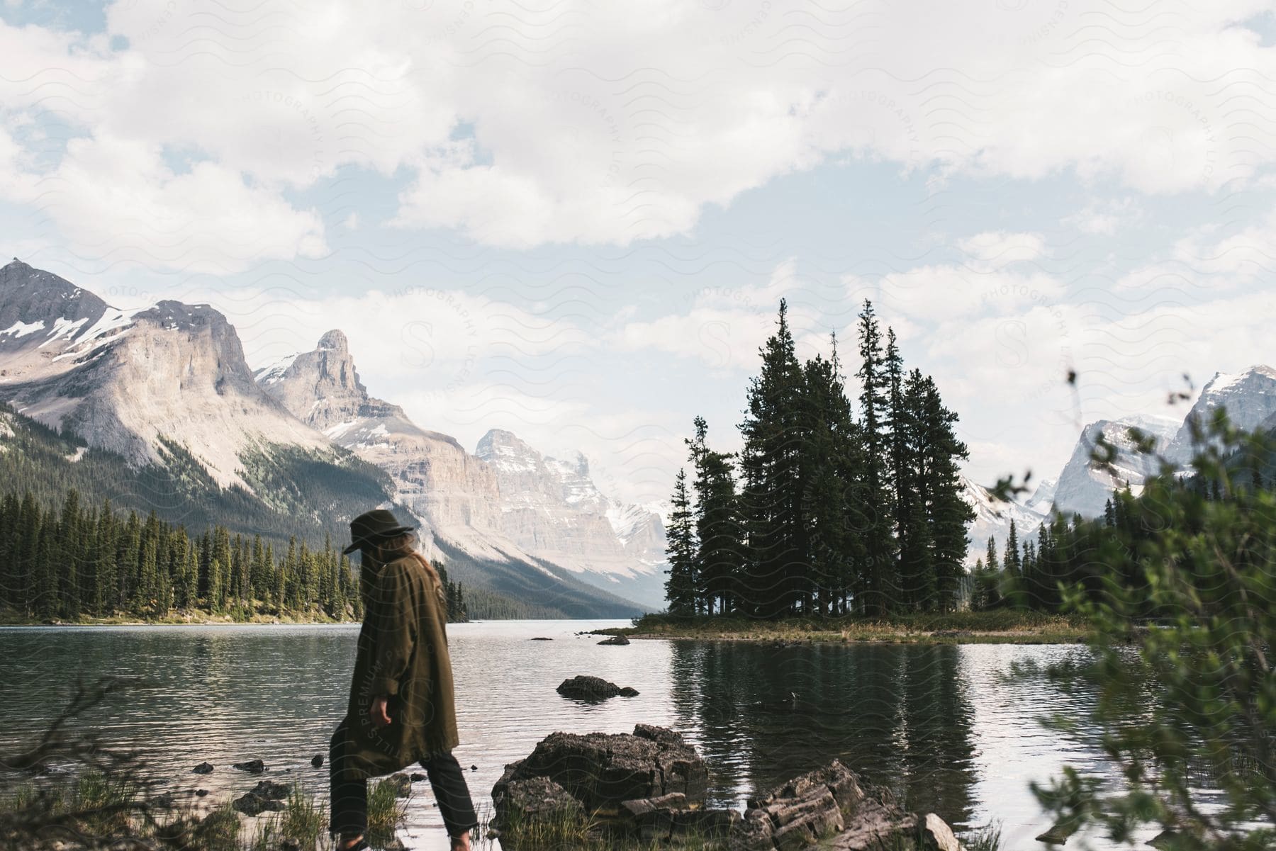 A woman walks along a rocky path with a river and mountains in the background