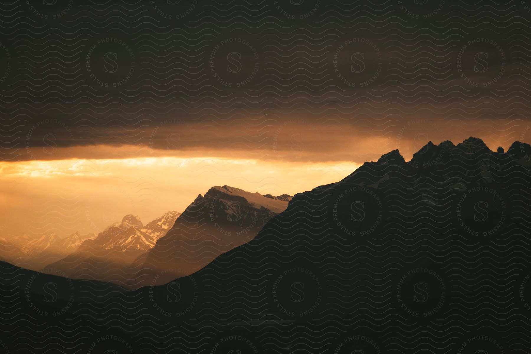 Silhouettes of mountains in a hazy orange sky with dark clouds overhead