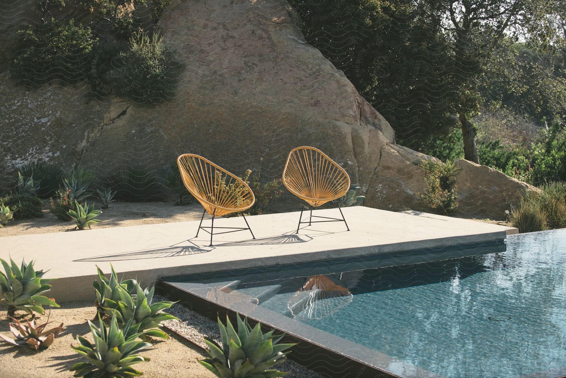 Two chairs on a deck next to a pool in a yard on a sunny day