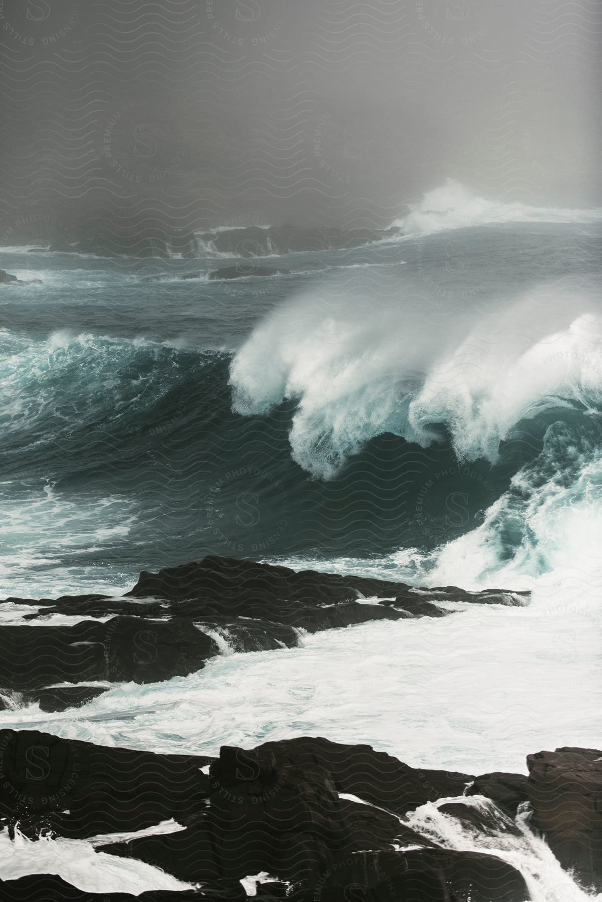 Strong ocean waves crashing onto a rocky coastline during a storm with low visibility