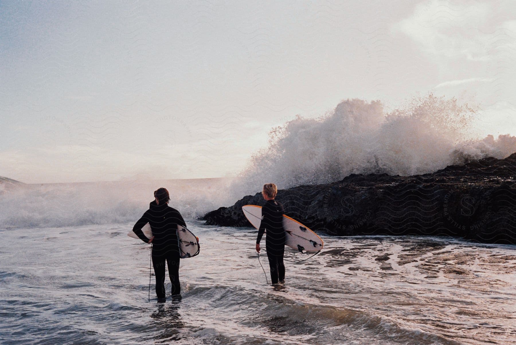 Two individuals holding surfboards observing the waves at an outdoor location