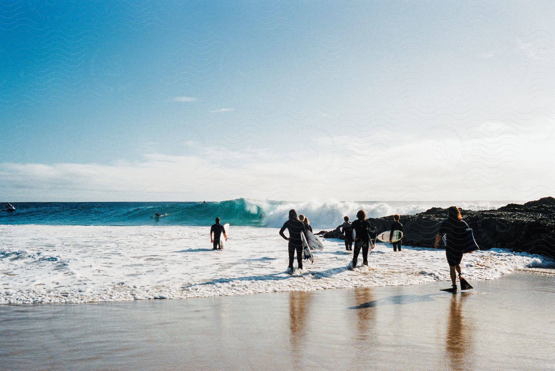 A group of males carry their surfboards into the ocean