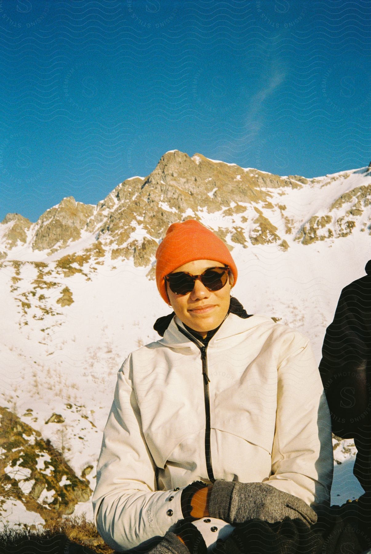 A woman wearing a jacket and glasses stands in a snowy mountain landscape during the day