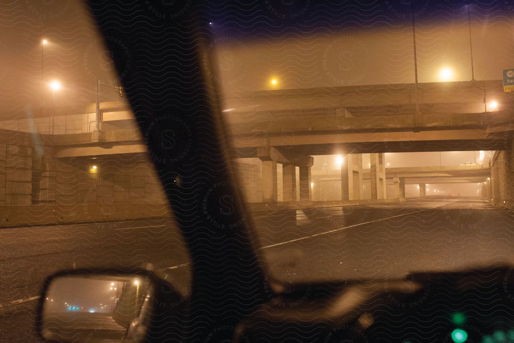 A closeup view of a bridge at night seen through the drivers side window of a car