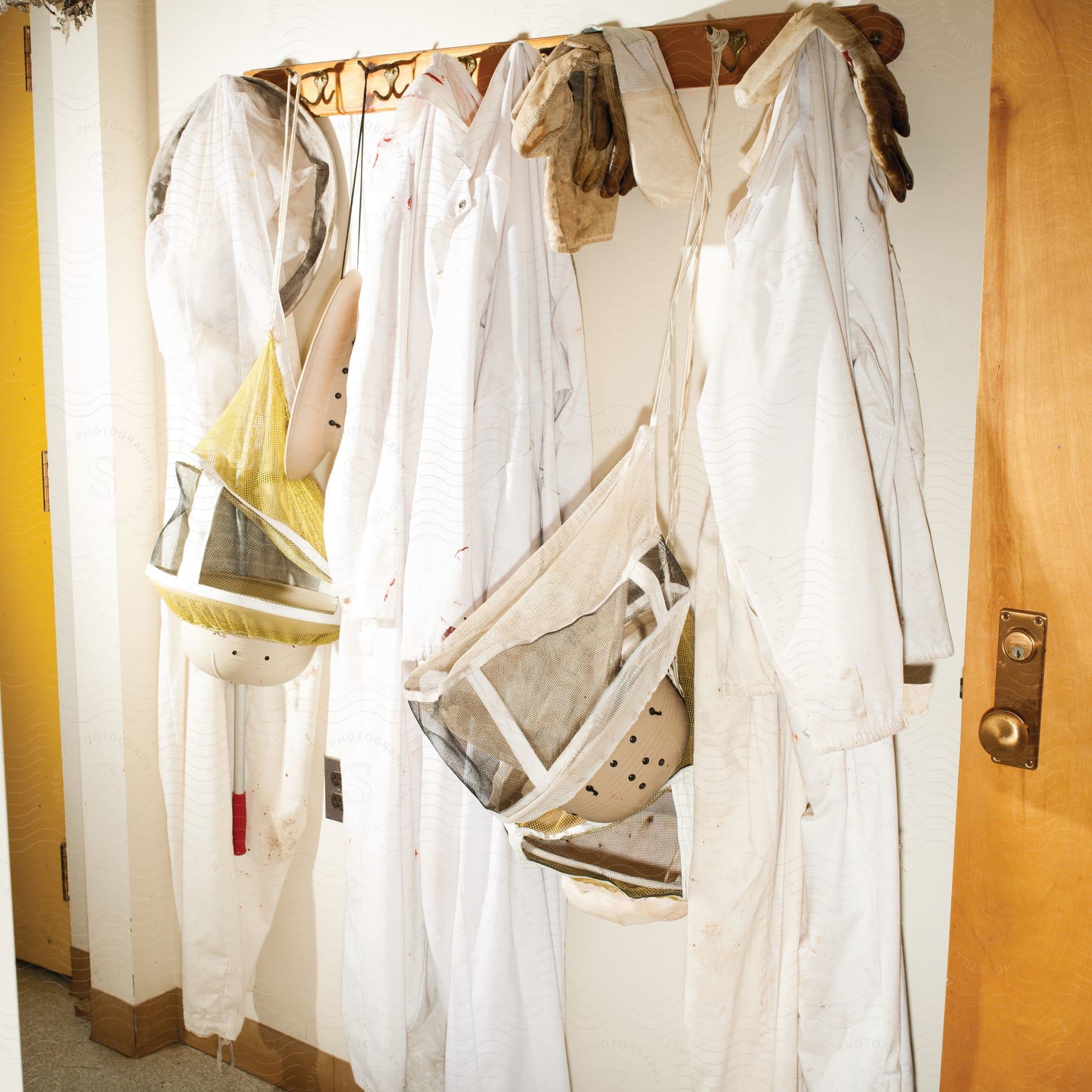 Beekeeper suits hanging on hooks against a white wall in a room