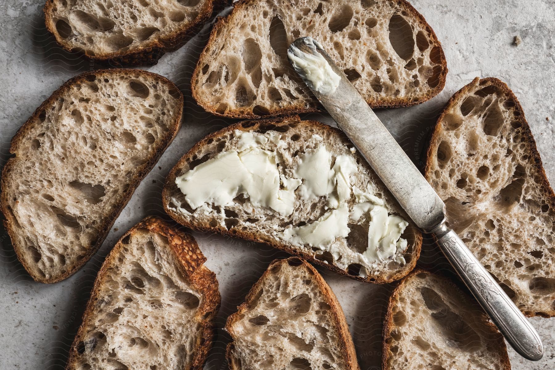 A buttered toast with a butter knife on it surrounded by seven other unbuttered toasts