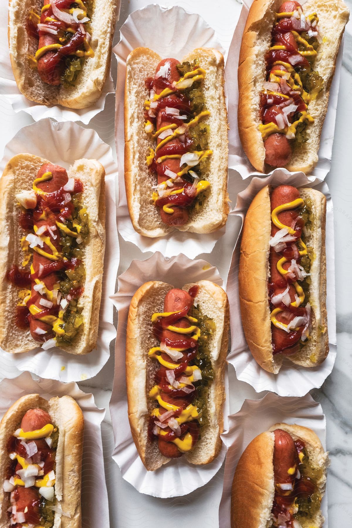 Eight hot dogs with ketchup mustard and onion on a marble countertop