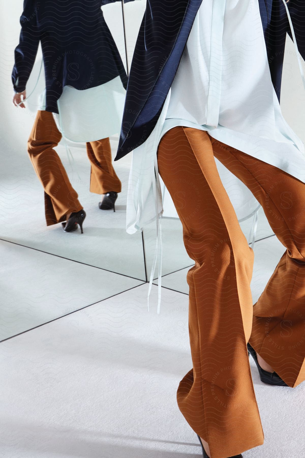 A woman posing indoors in fashion clothes with a mirror reflecting her image behind her