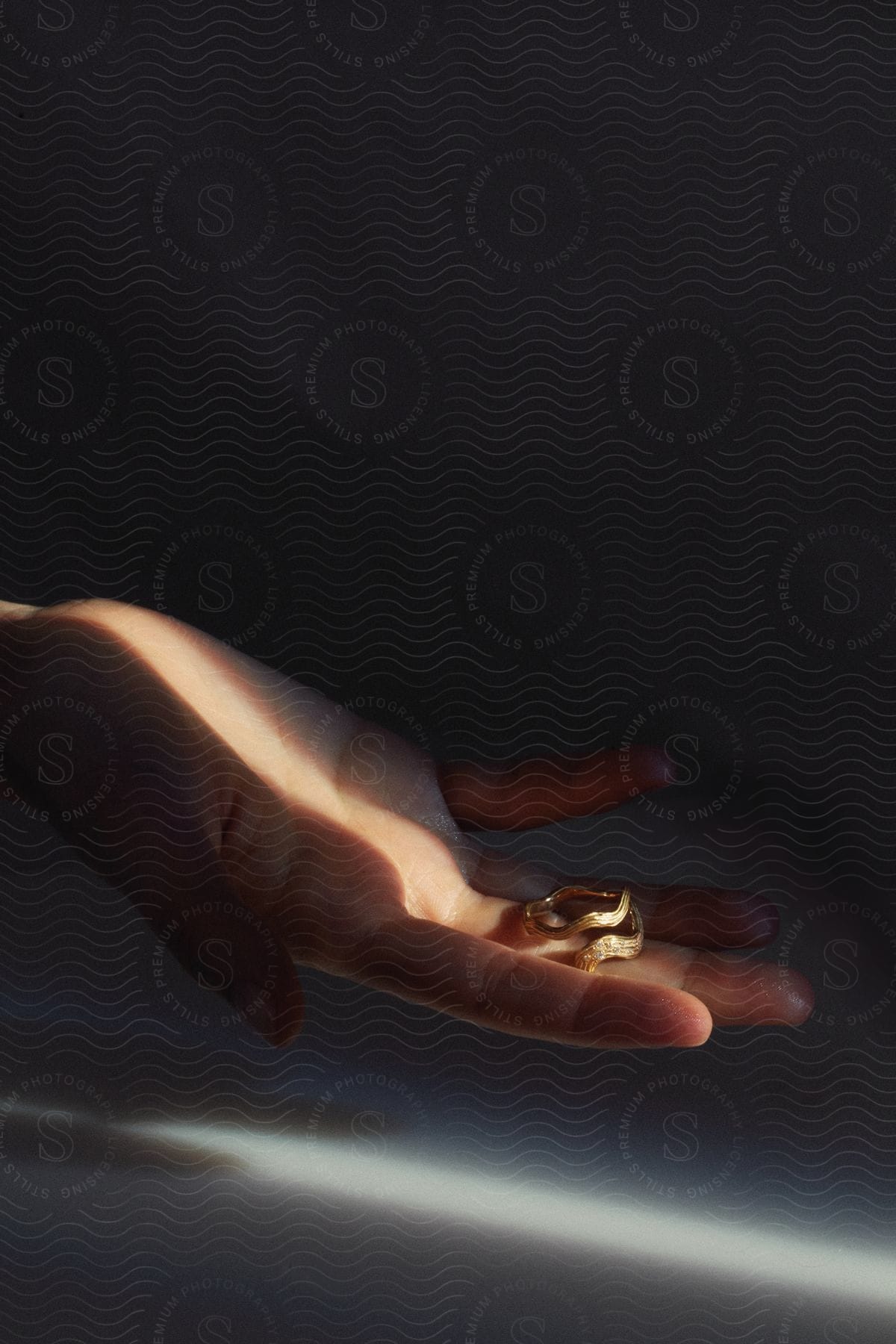 Stock photo of a hand holding a ring in a dimly lit room with a single narrow light