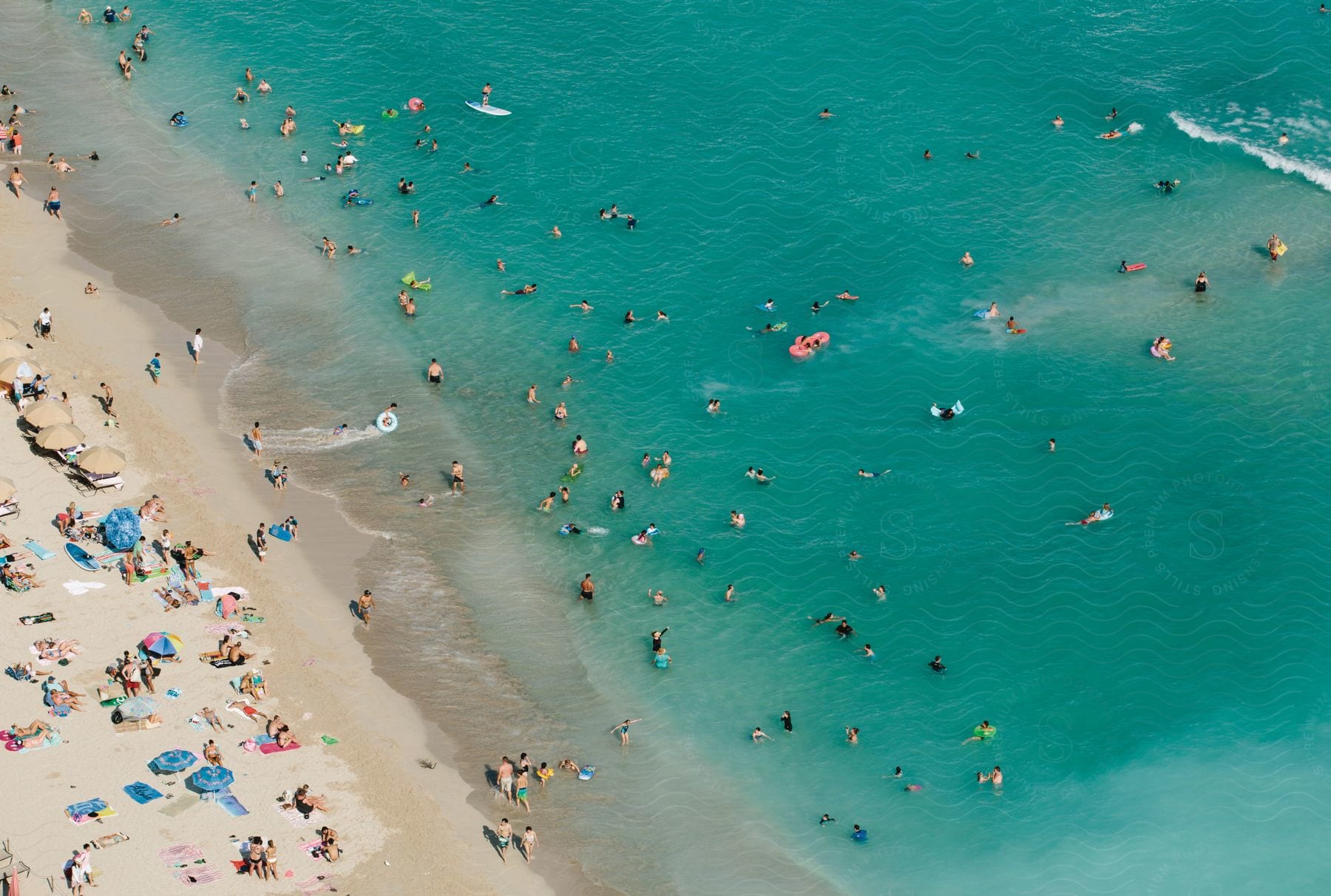 A wide shot of people swimming walking and sitting on the beach by the shore