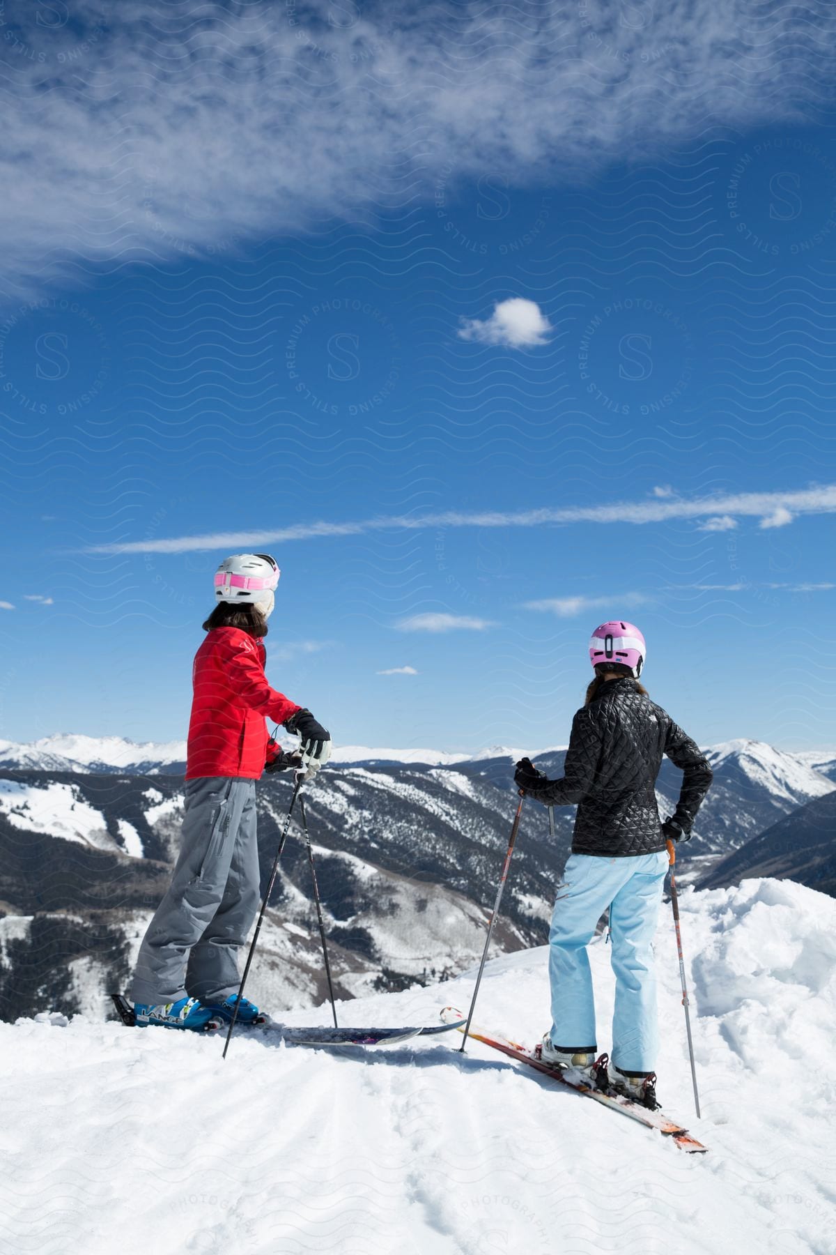 Two women skiiers stand at the top of a mountain preparing to ski down