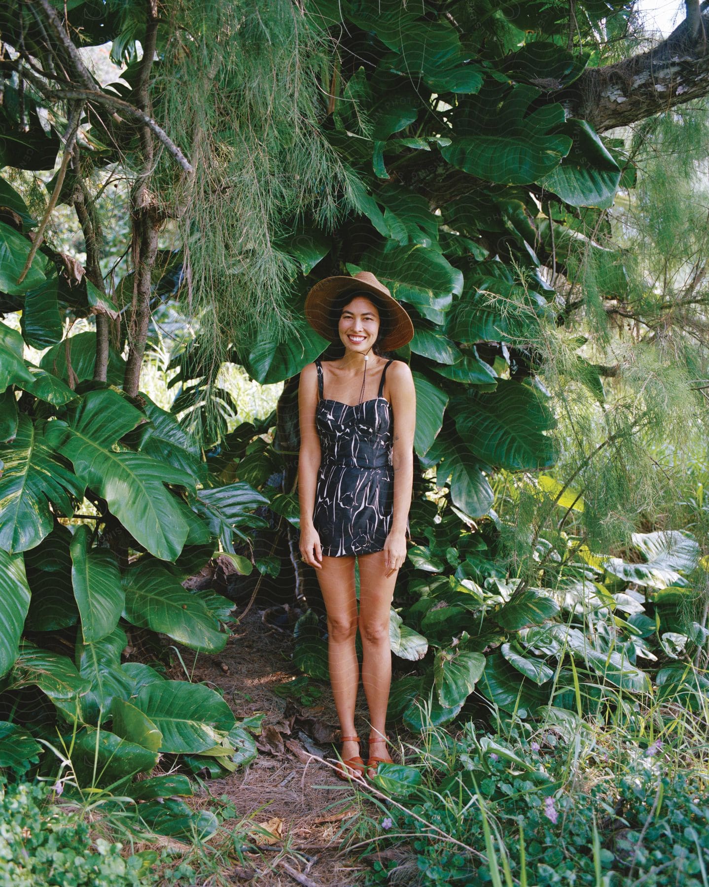 A woman standing in front of a large leafy plant wearing a romper