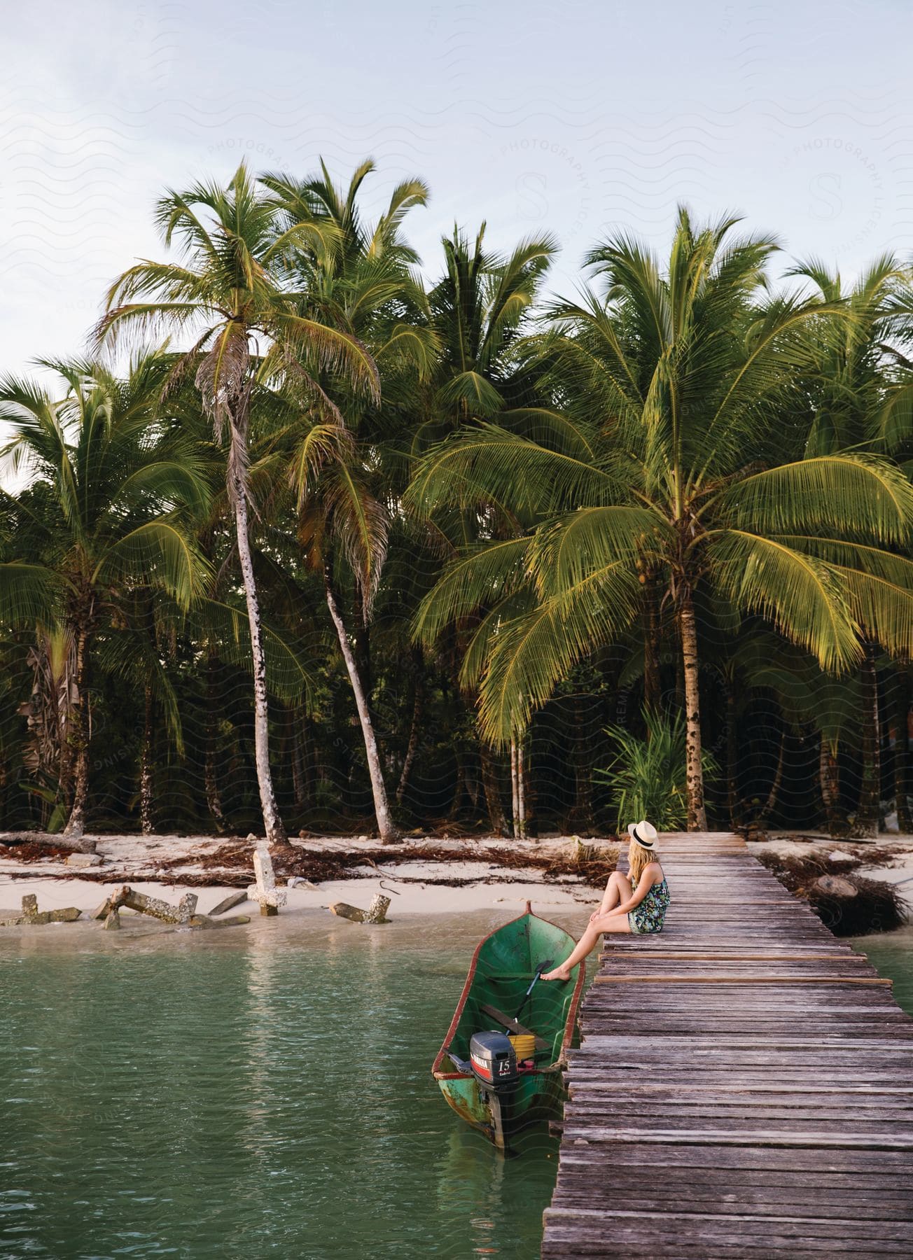 A woman sits on a pier next to a motorboat on a tropical beach