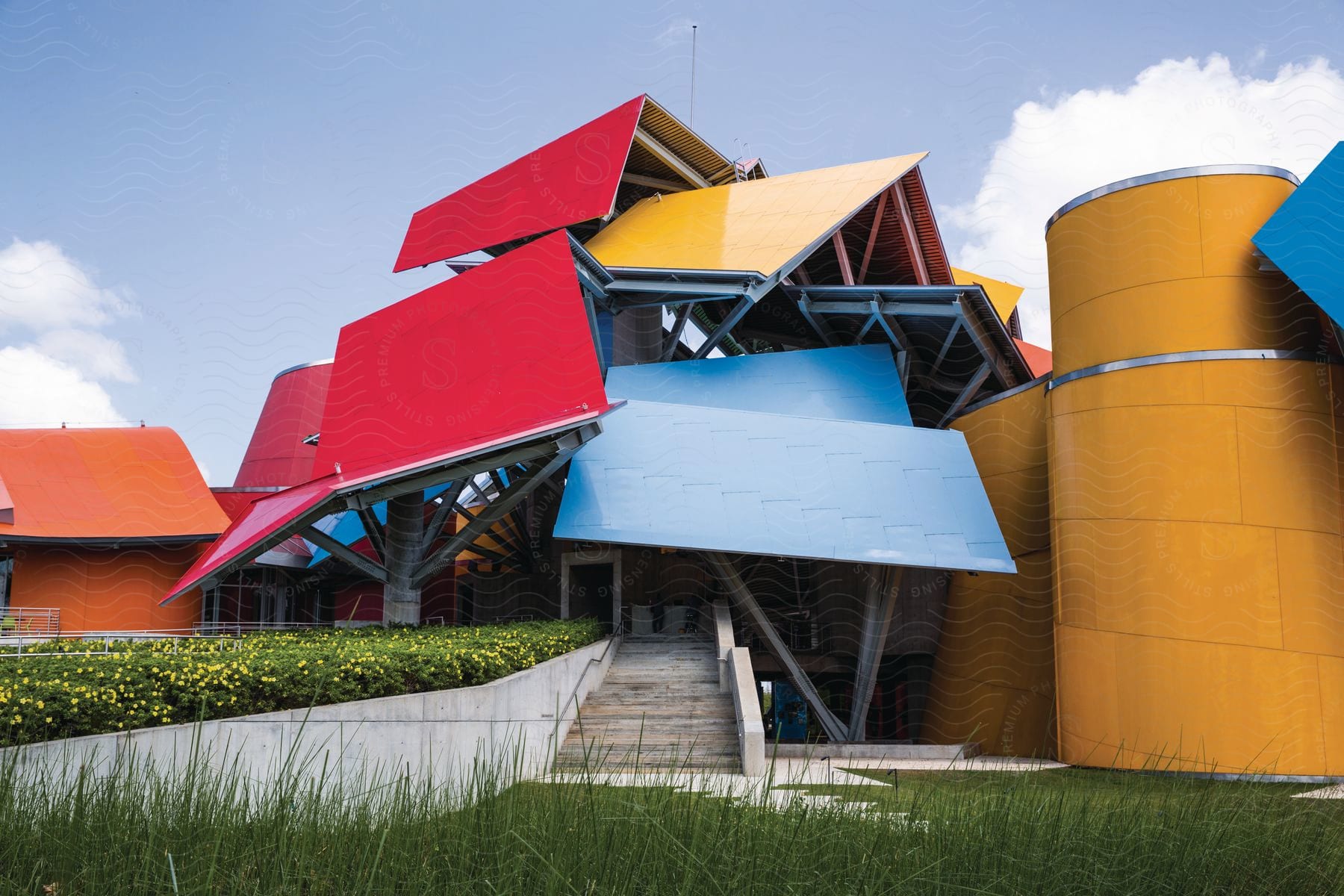 A colorful building with abstract angles against a blue sky surrounded by green grass and foliage