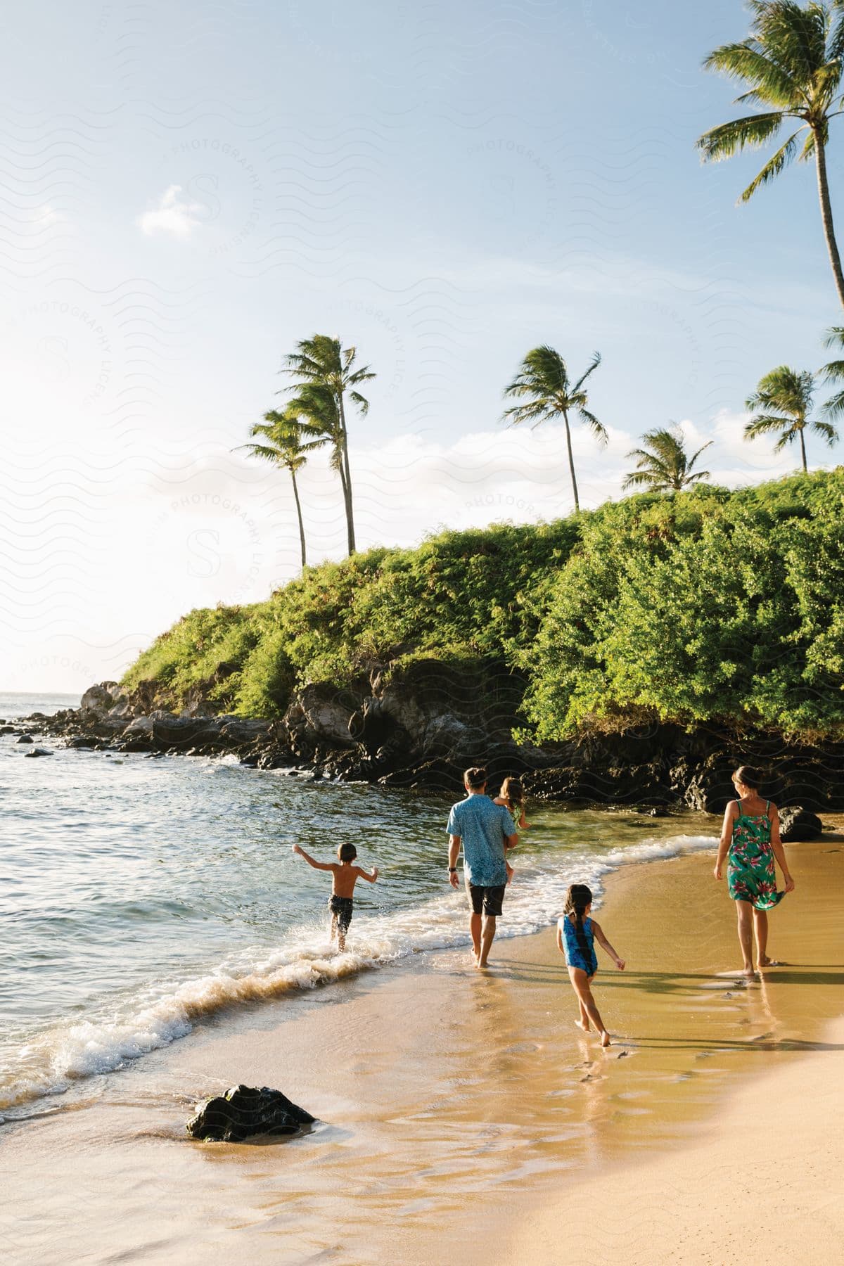 Stock photo of a family of 5 plays on the beach with a grassy cliff beyond them