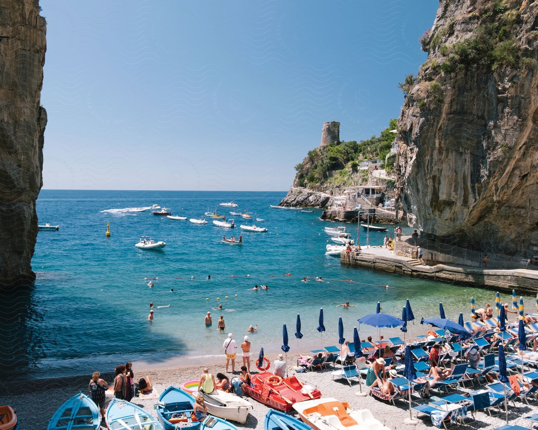 A beach with many people relaxing swimming and riding in boats