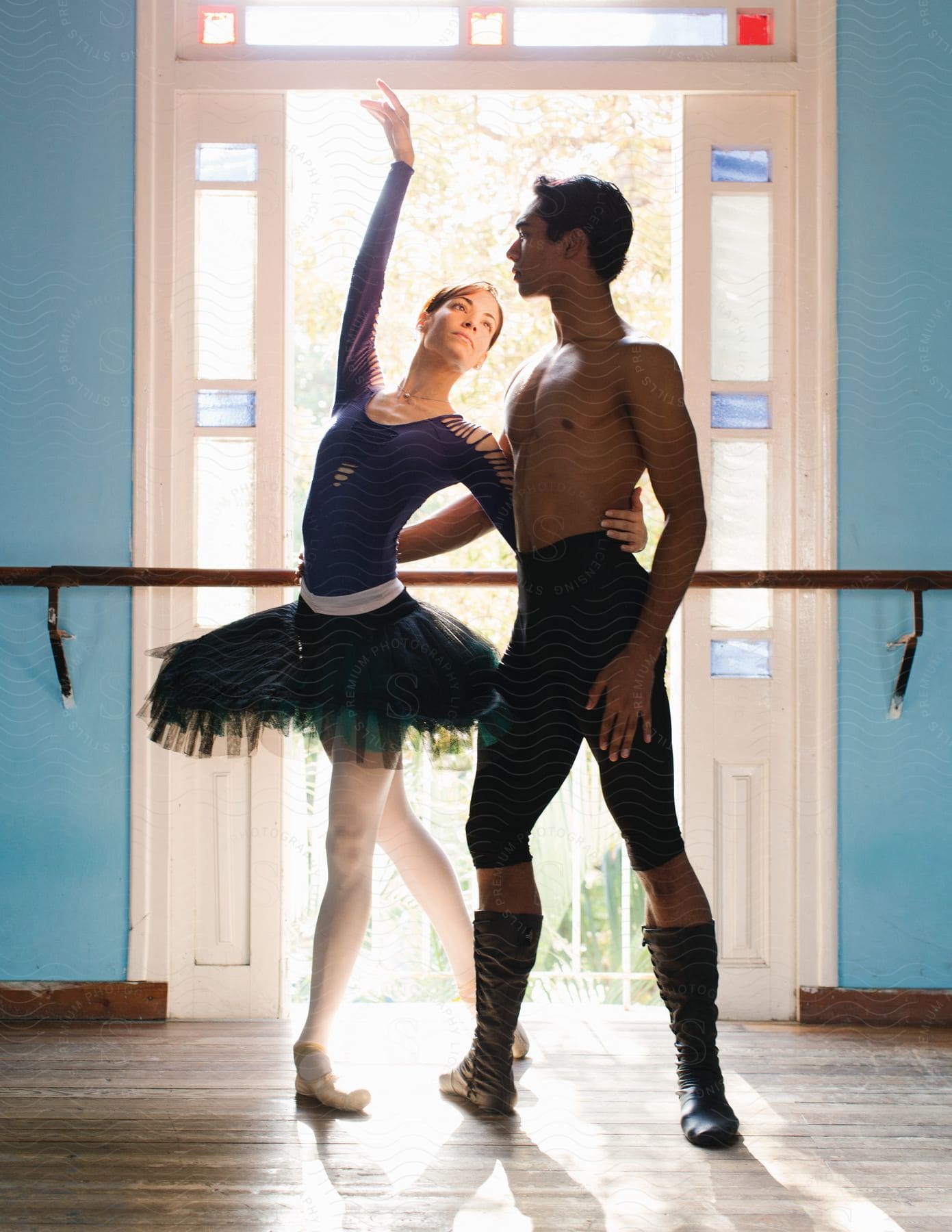 Two ballet dancers perform a dance in front of an open door with stained glass panels