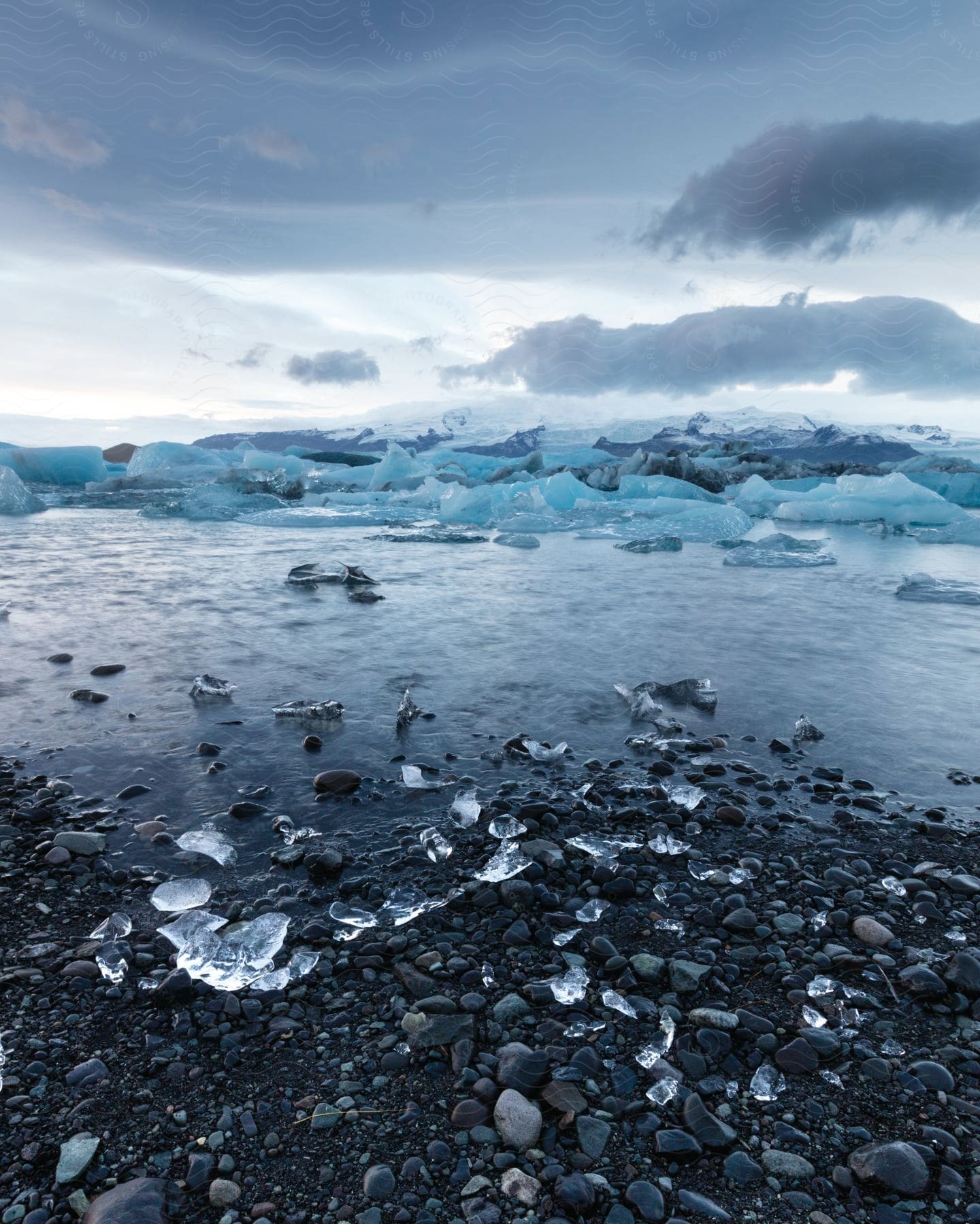 Sea ice floats off ice and pebble strewn coast under dark clouds