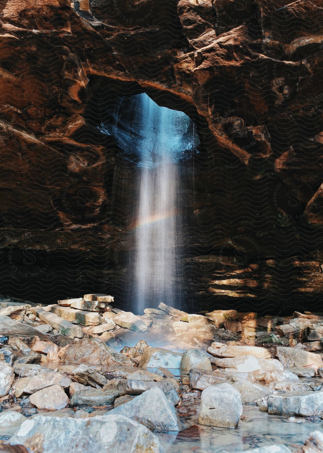 Water flowing through a hole in a rock into a rocky cavern pool below in a natural landscape