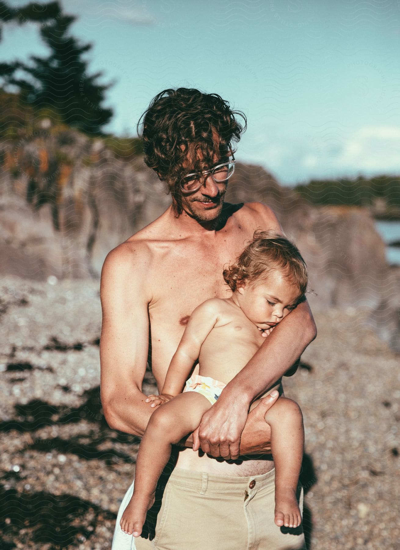 A man holds his sleeping baby boy on the beach