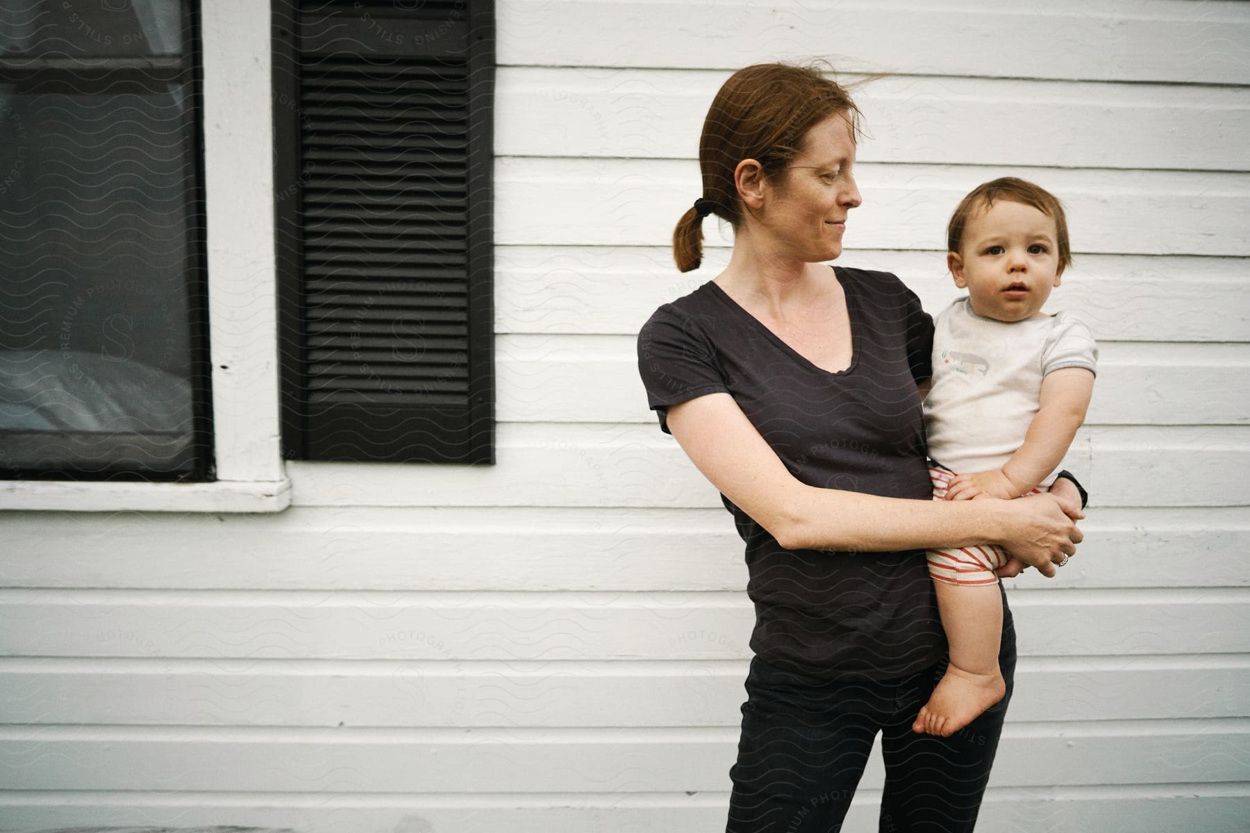 A woman holds a young child in front of a house