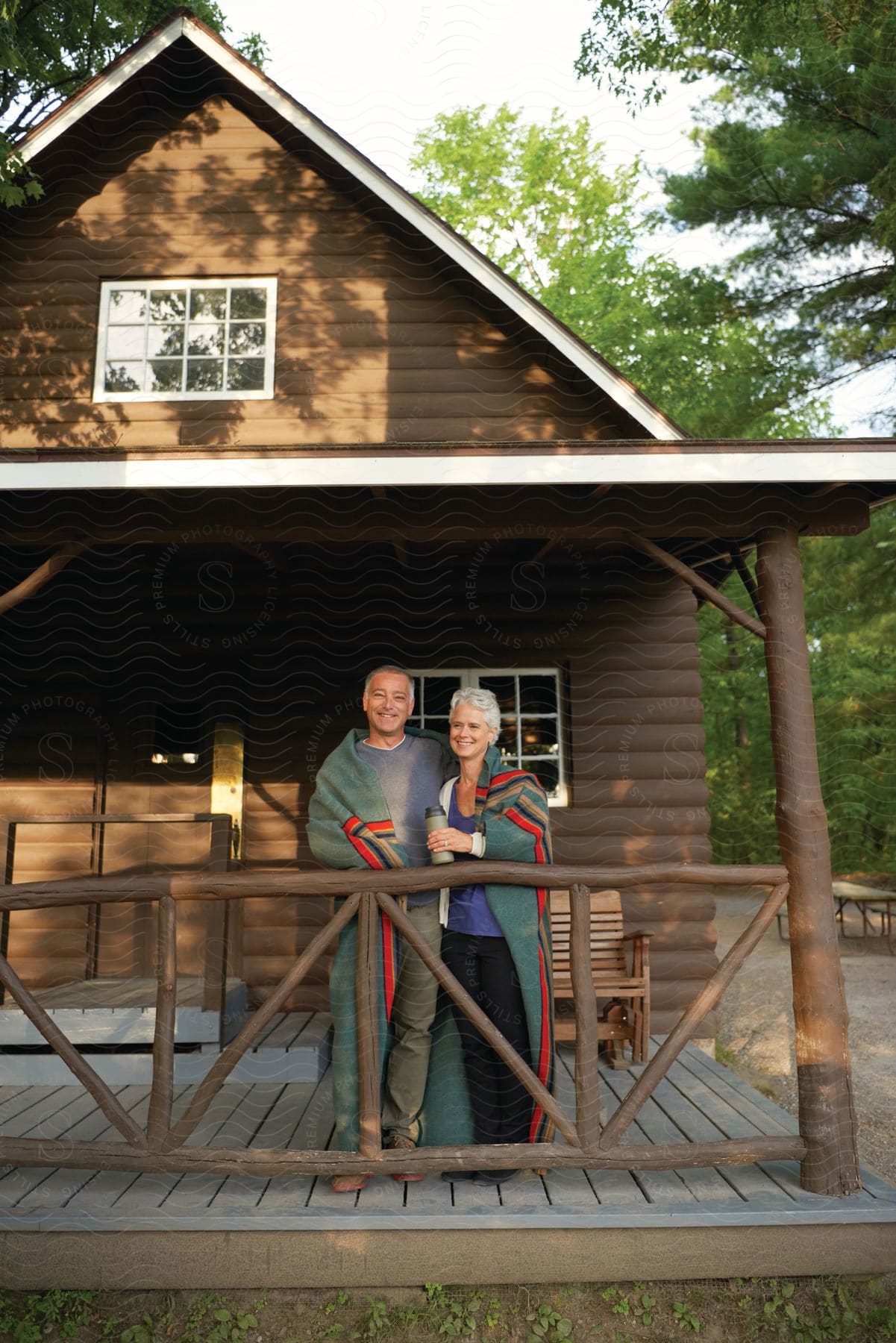 An older couple sits together on the porch of their log cabin