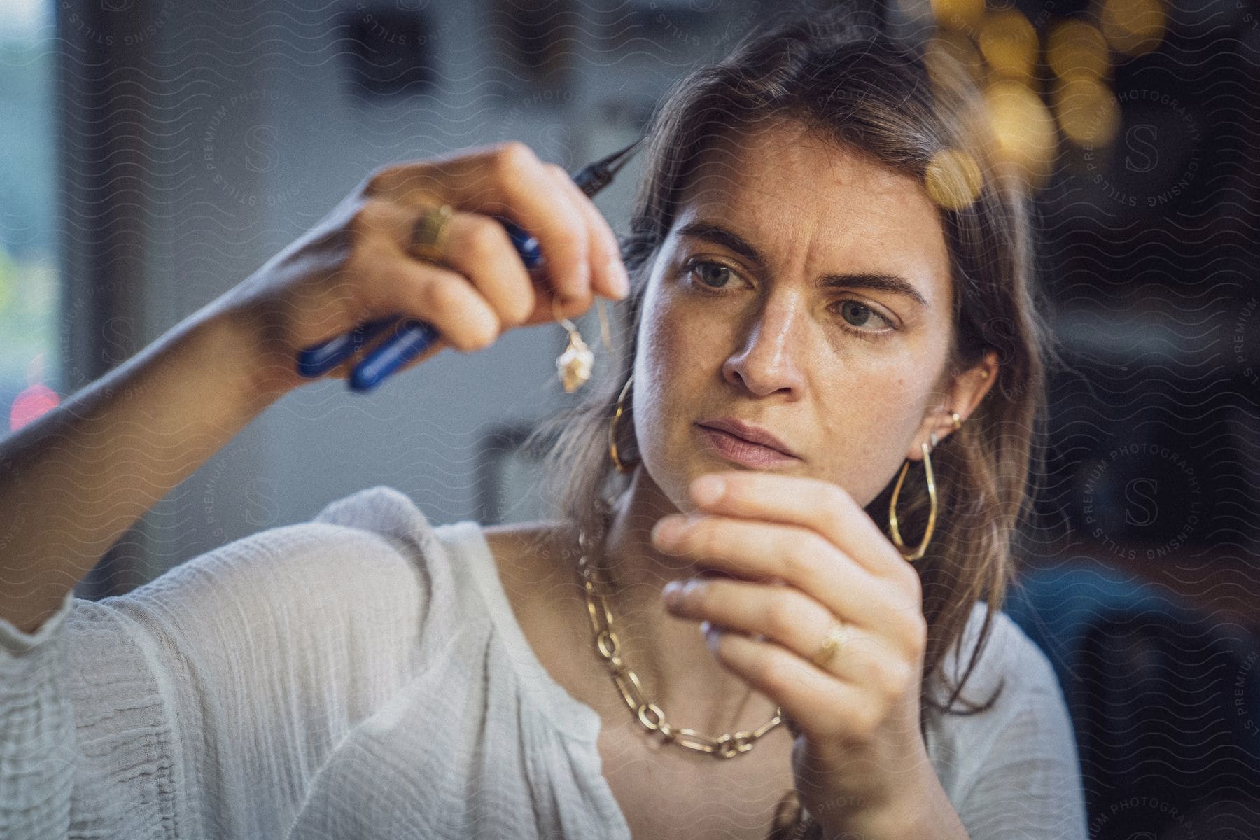A woman in her 40s examines jewelry with pliers