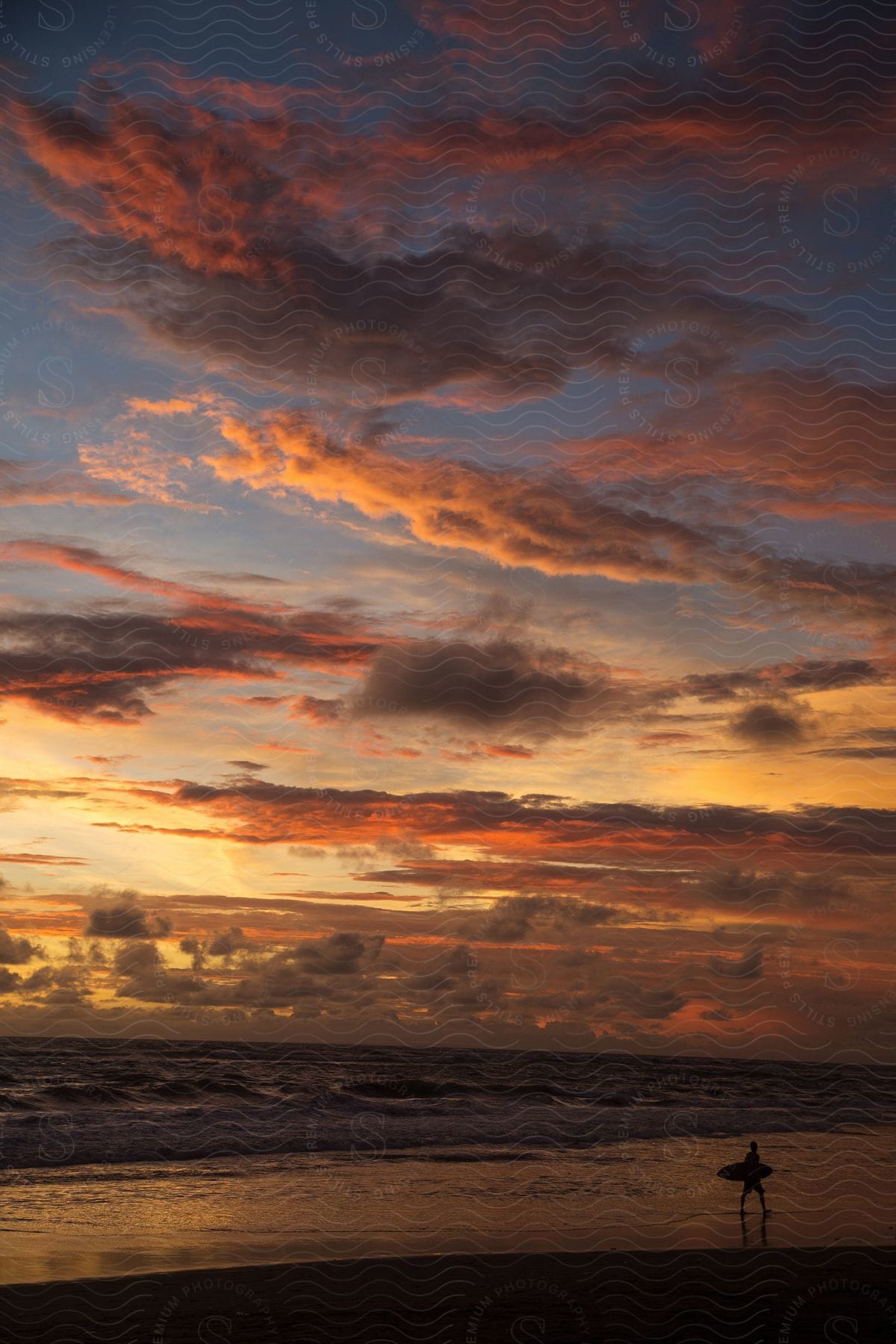 A person standing on a beach during sunset with a red and orange sky in the background