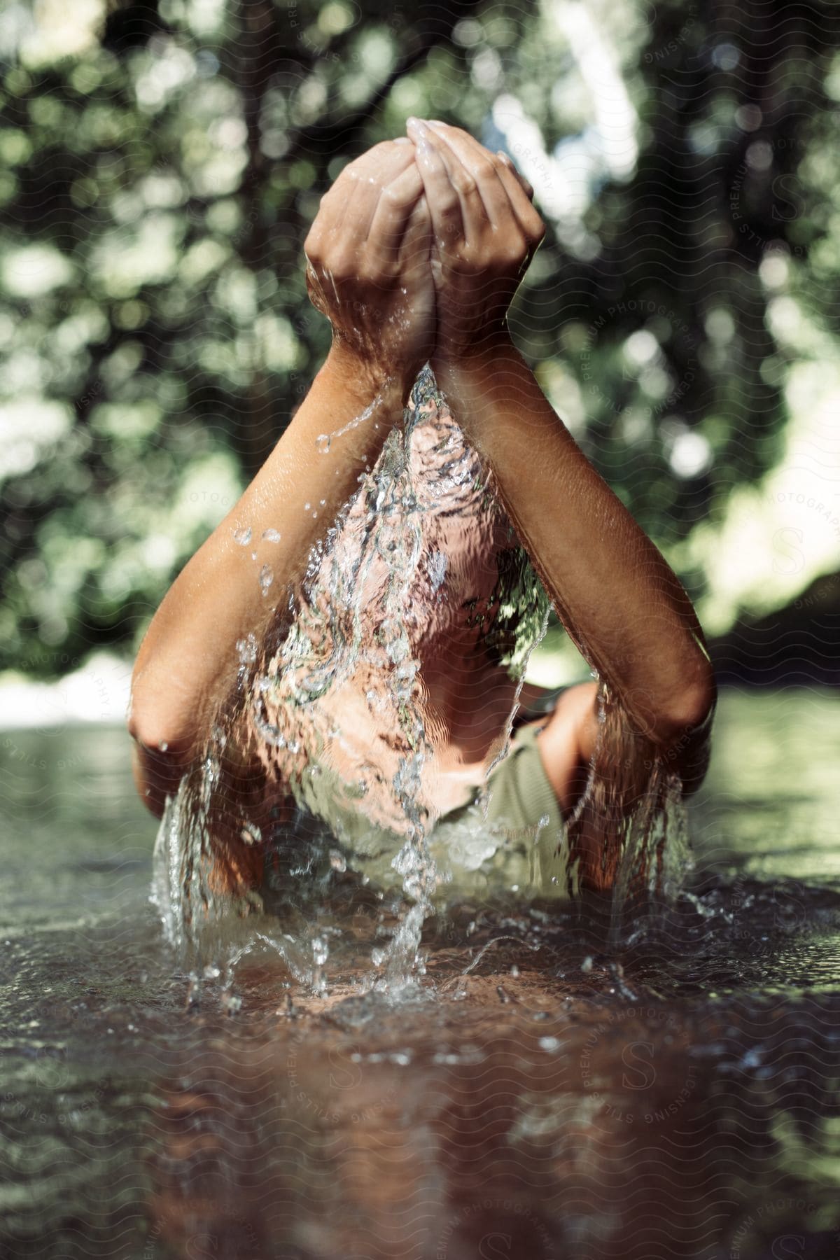 A person in a green tank top shields their face from water droplets as they stand in the water