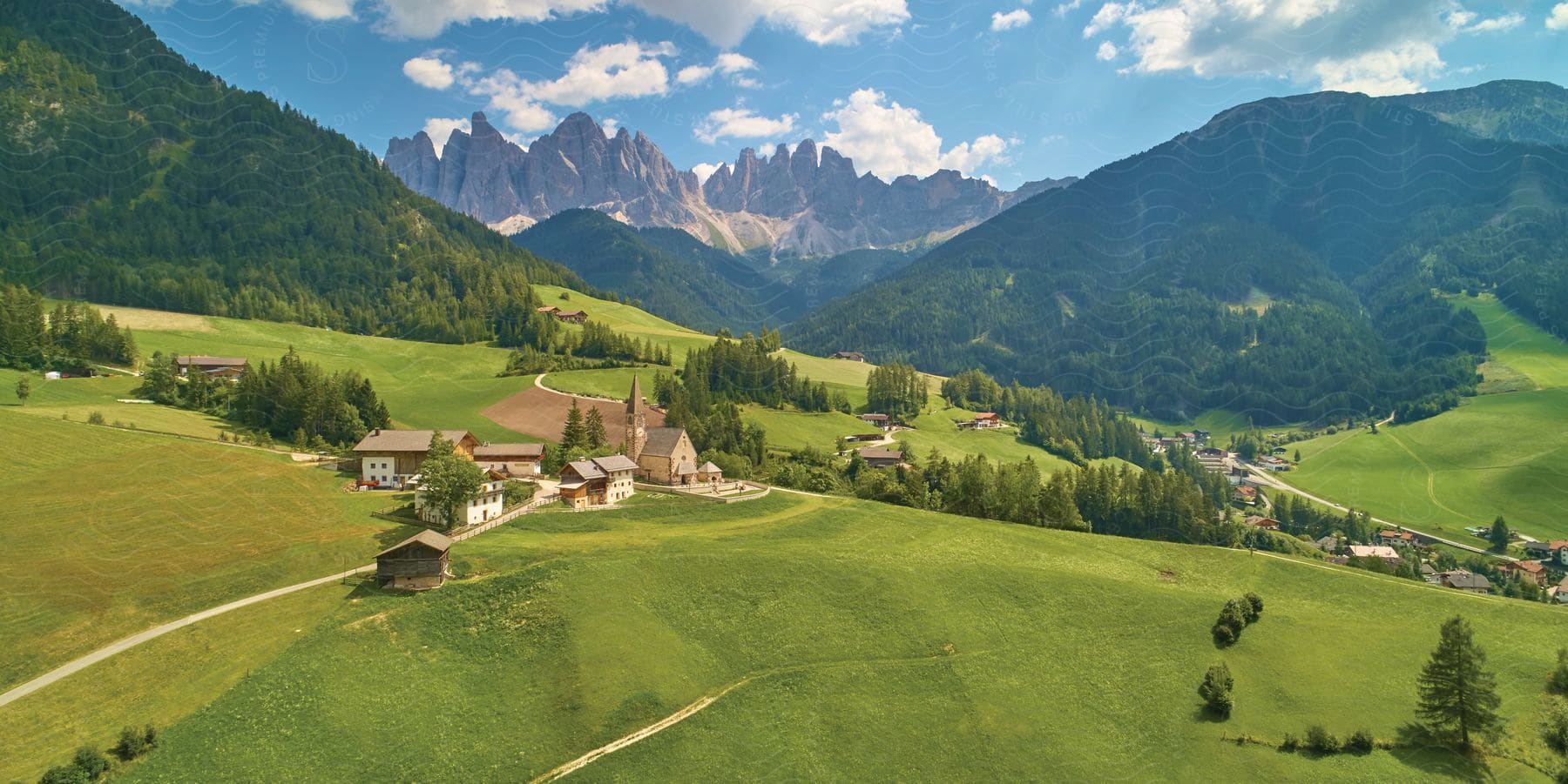 Road drives through town nestled between forest covered mountains and a jagged mountain on the horizon