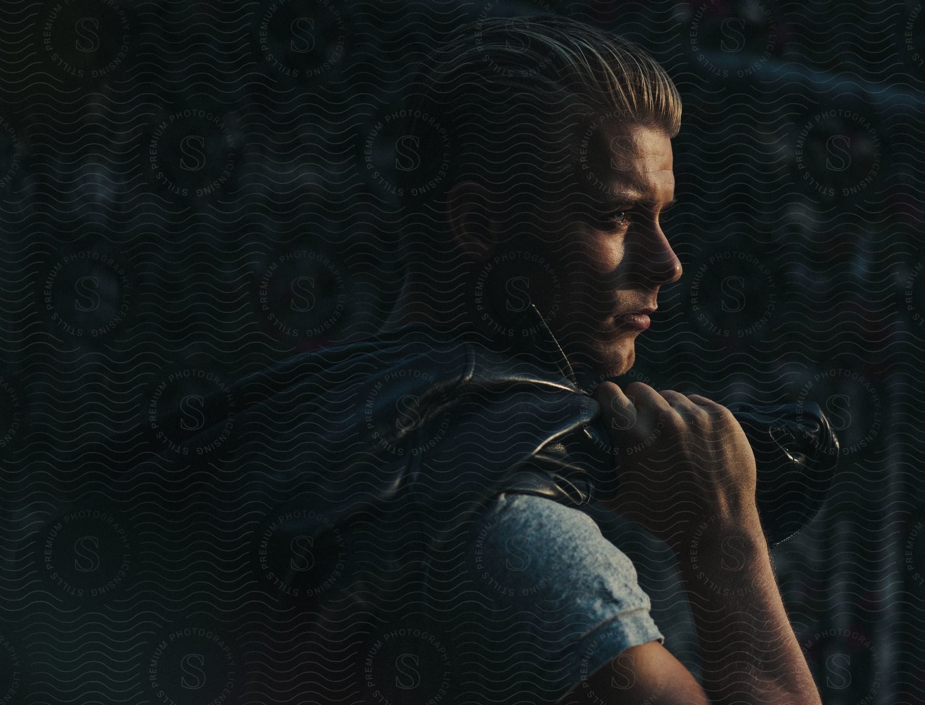 Blonde male model posing with a jacket draped over his shoulders for a photoshoot