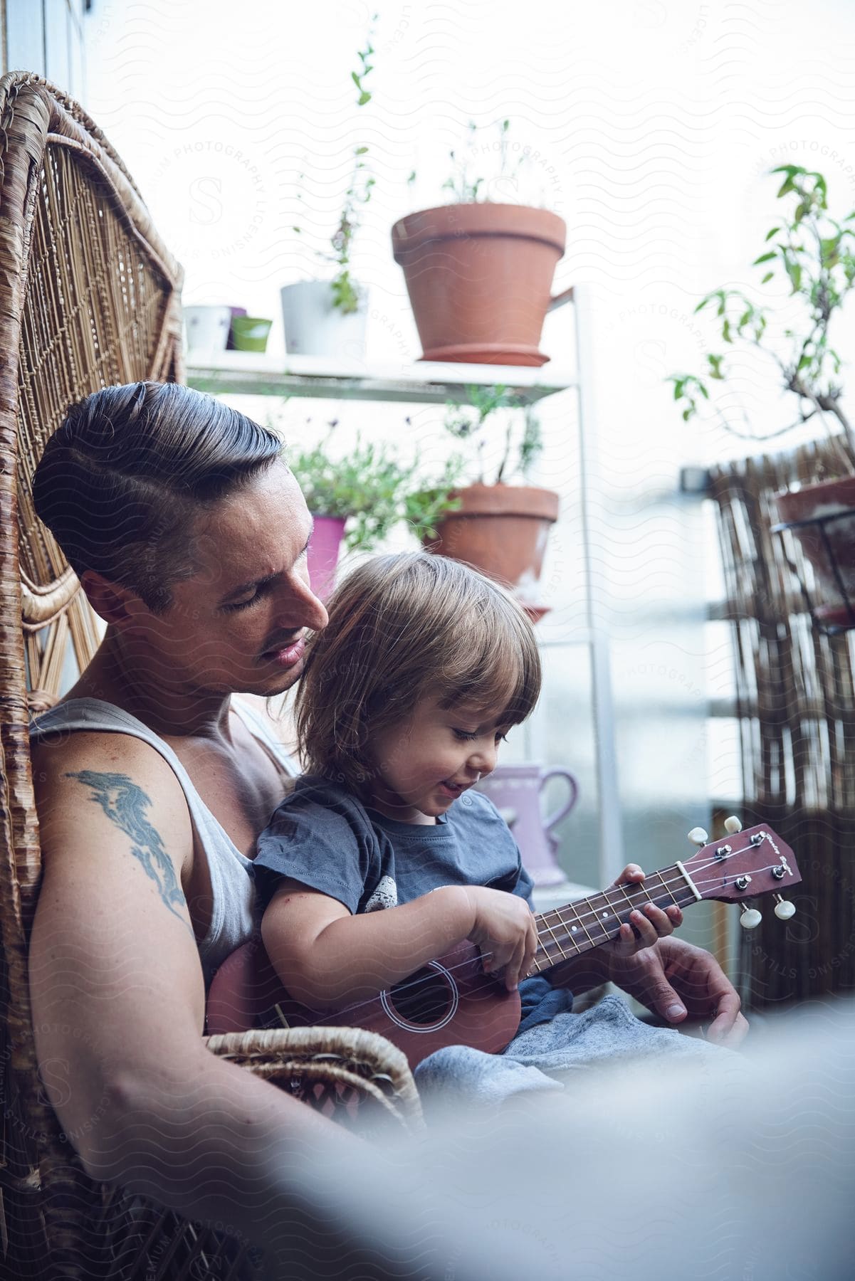 Father and son sitting on a chair with the boy playing the ukulele