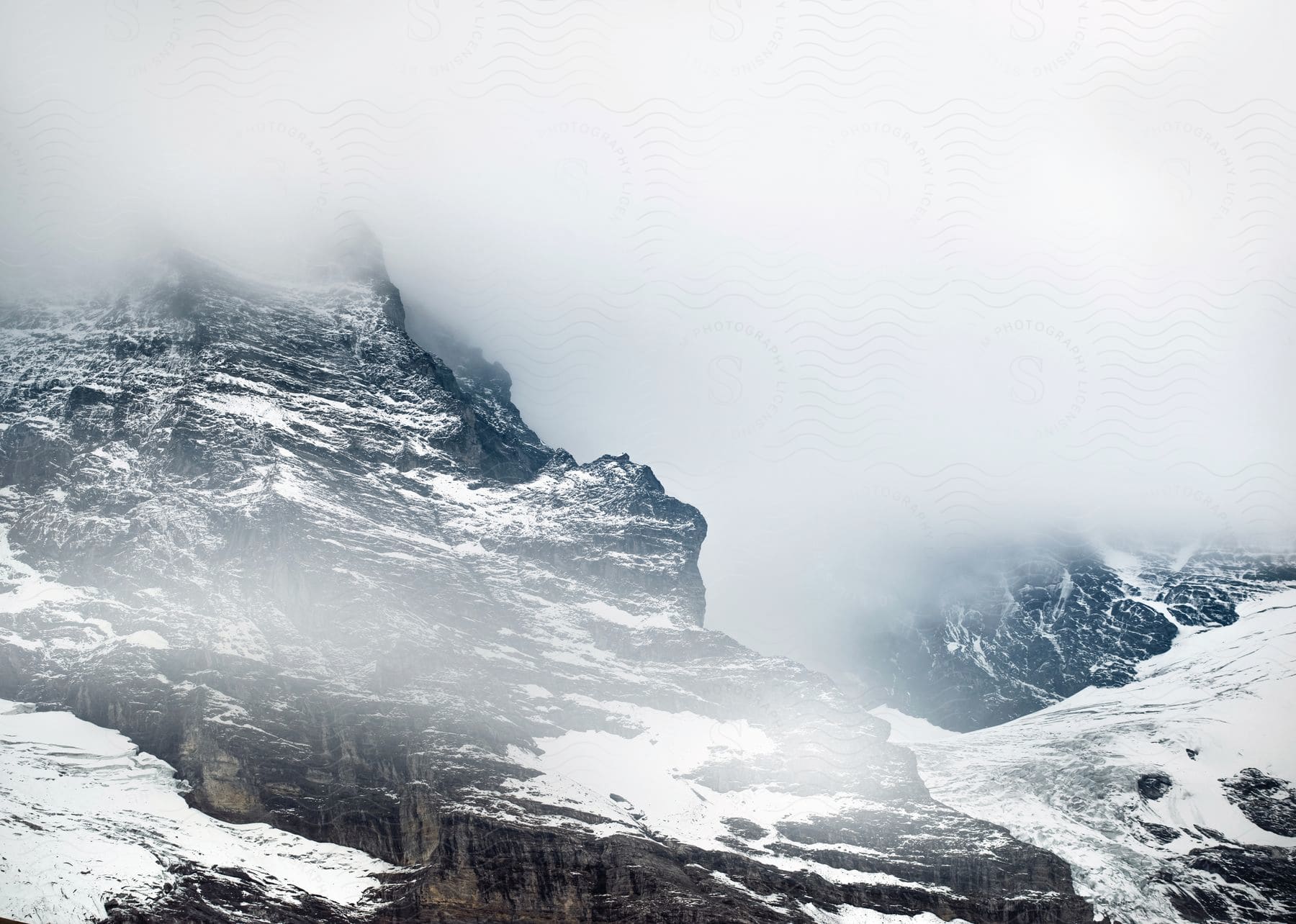 A tall mountain covered in ice surrounded by swirling winds and thick fog