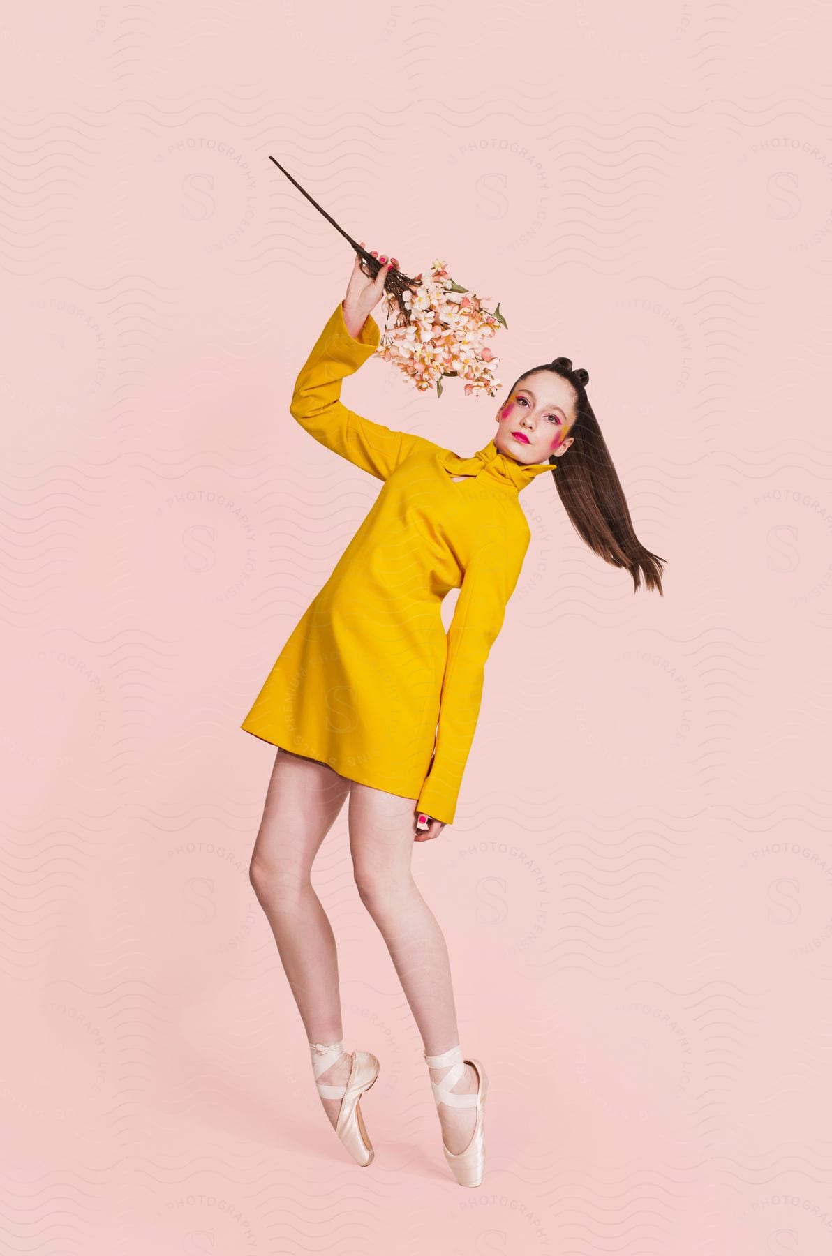 A woman in a yellow dress and ballet shoes poses while holding flowers