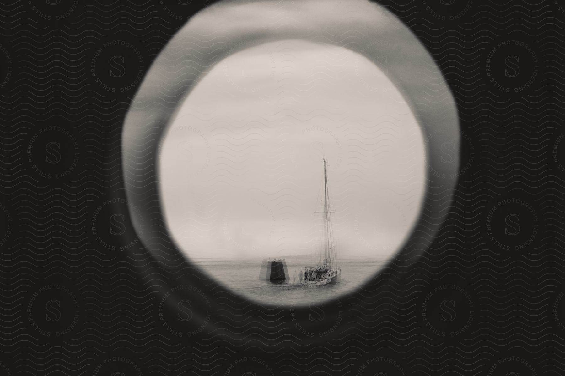 A sail boat is visible through a port hole on a foggy day