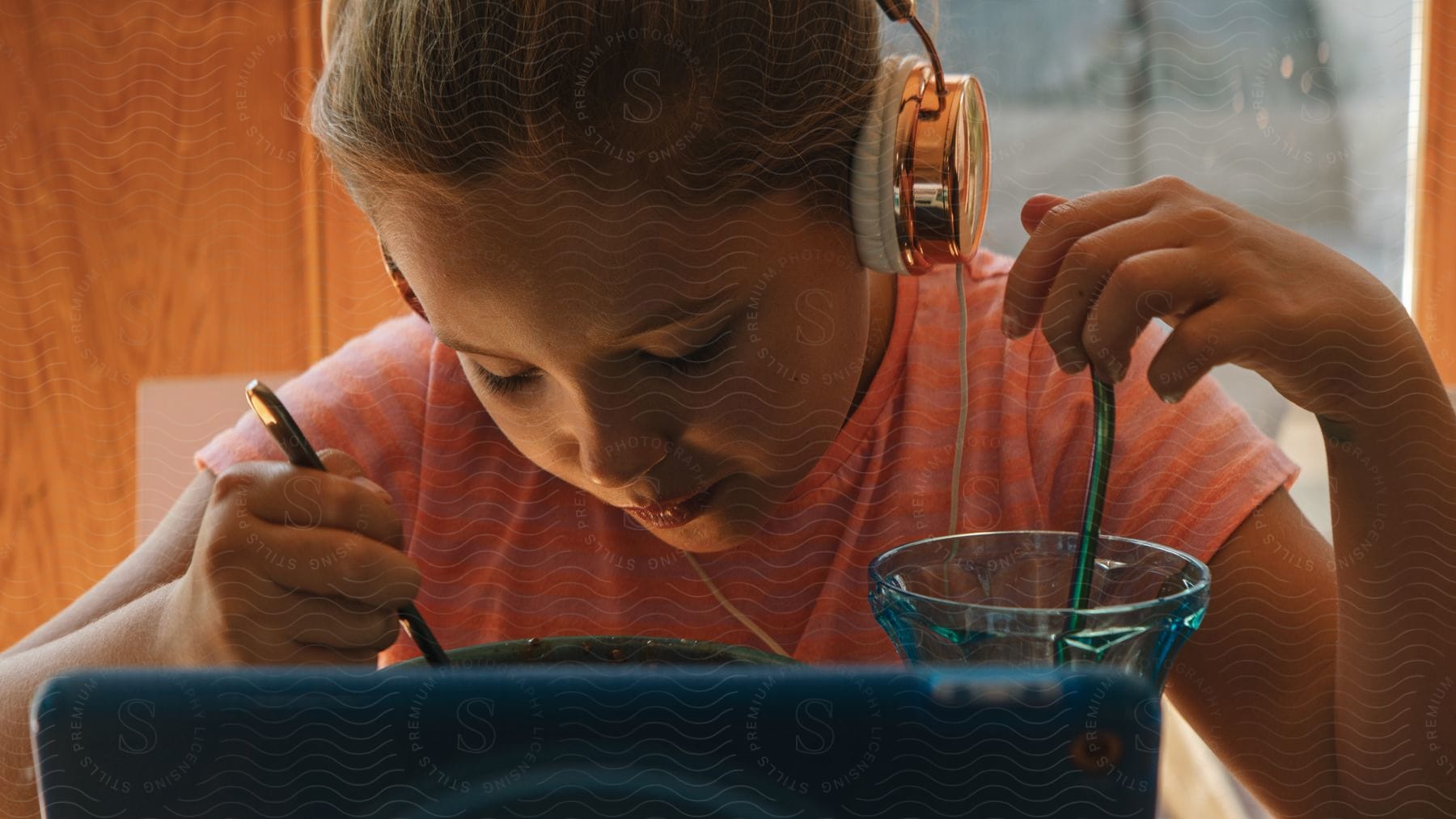 A young girl using headphones and a computer while eating and drinking