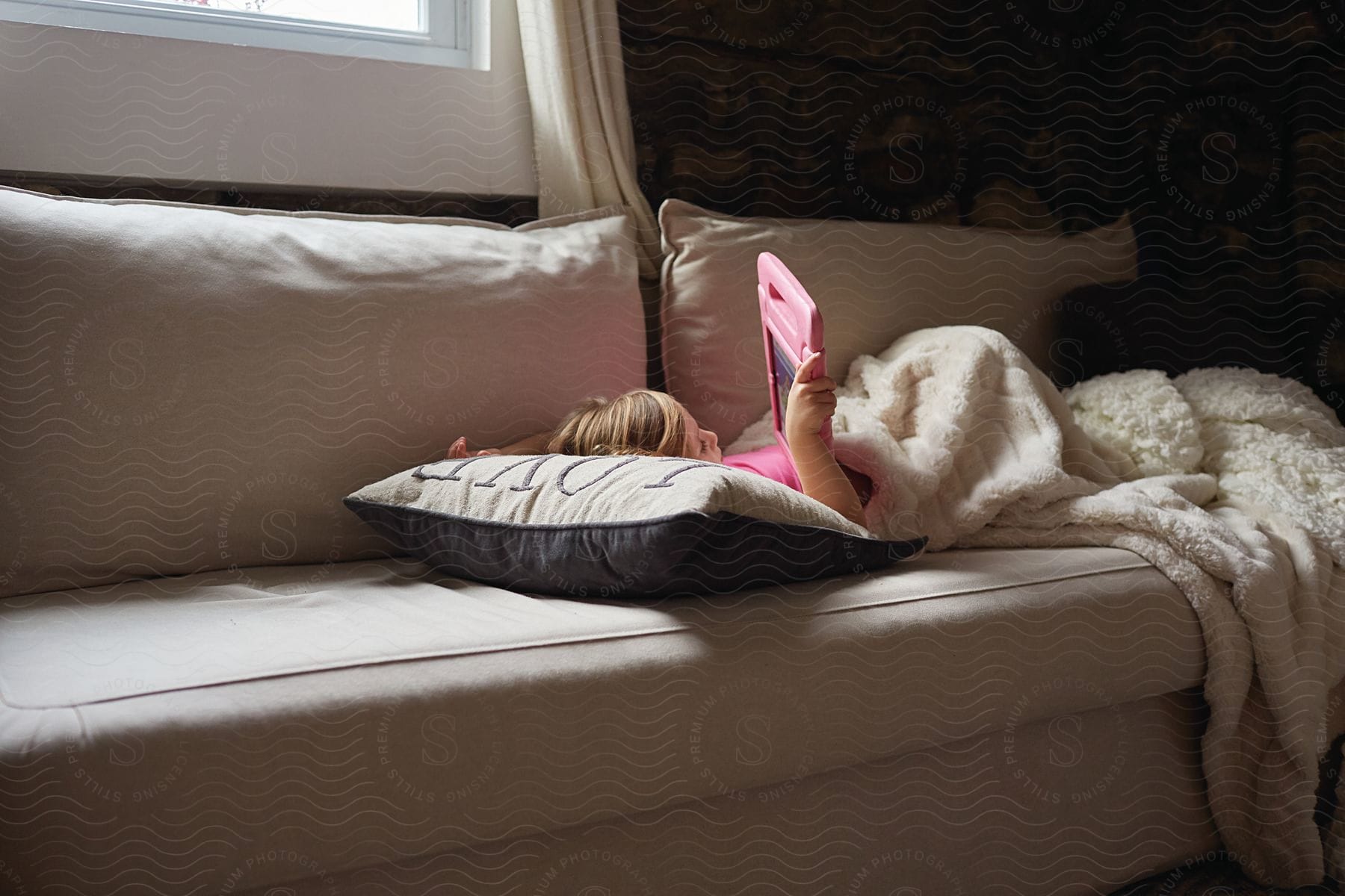 A child lying on a sofa using a tablet