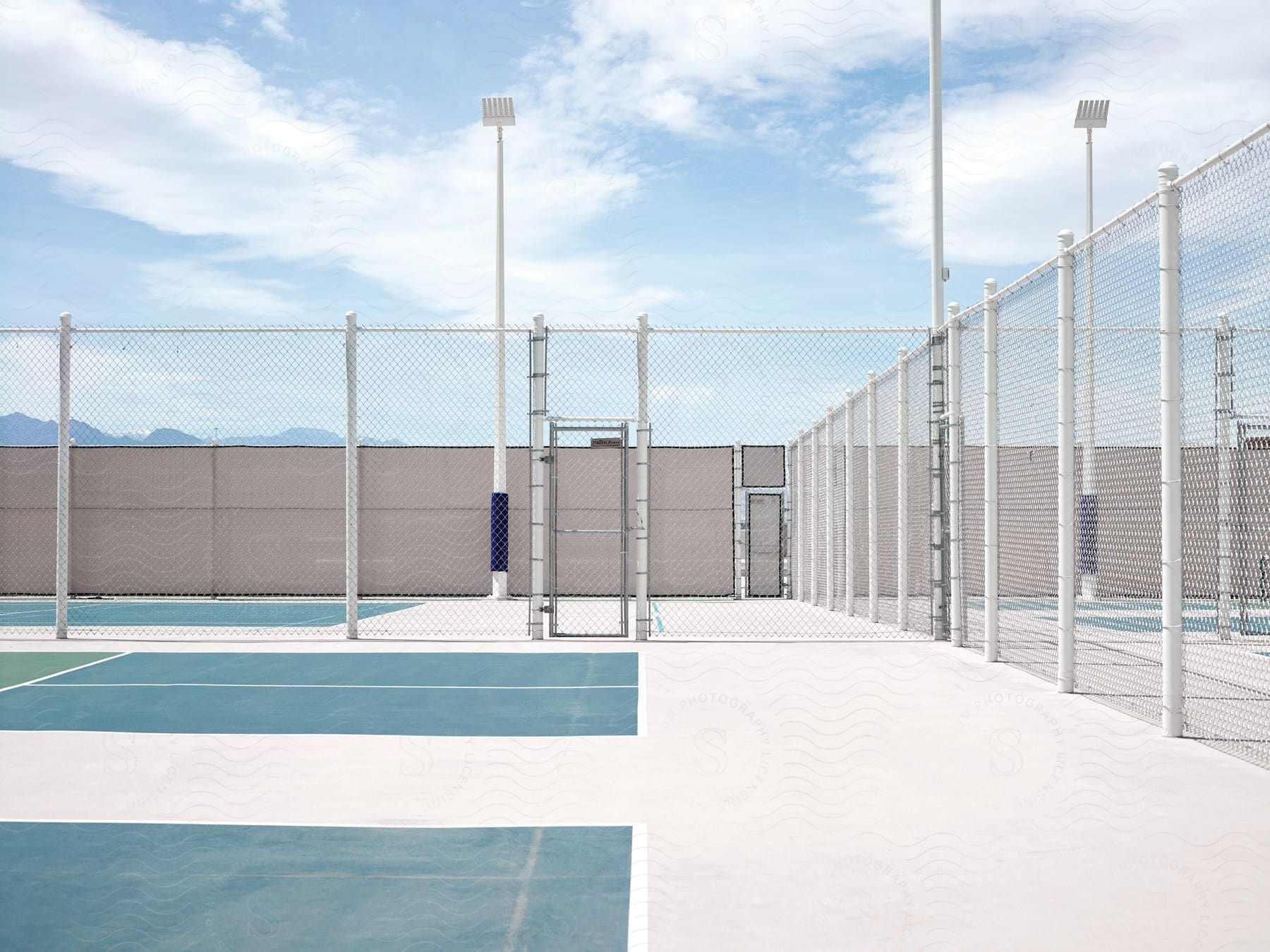 A ground with a net fence and light poles under a clear sky in the afternoon