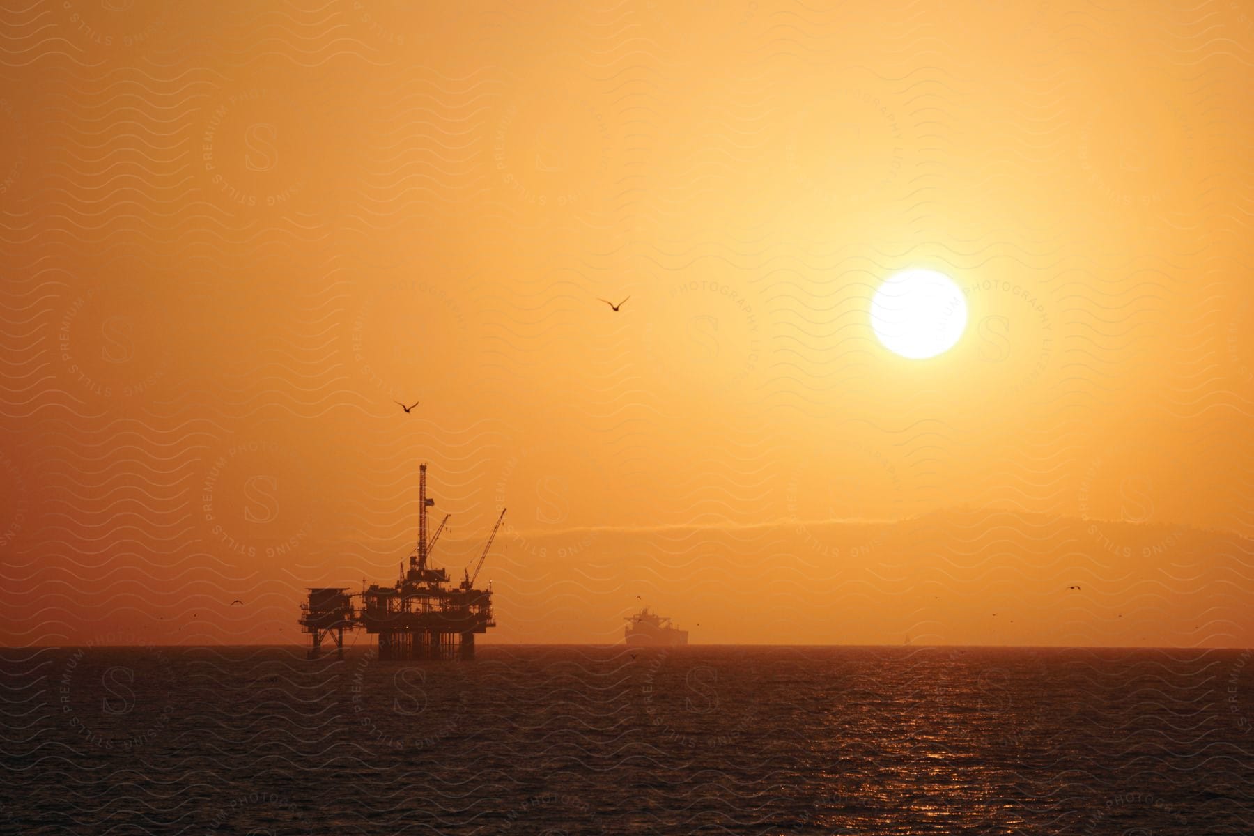 An oil rig in the open ocean with a ship sailing away