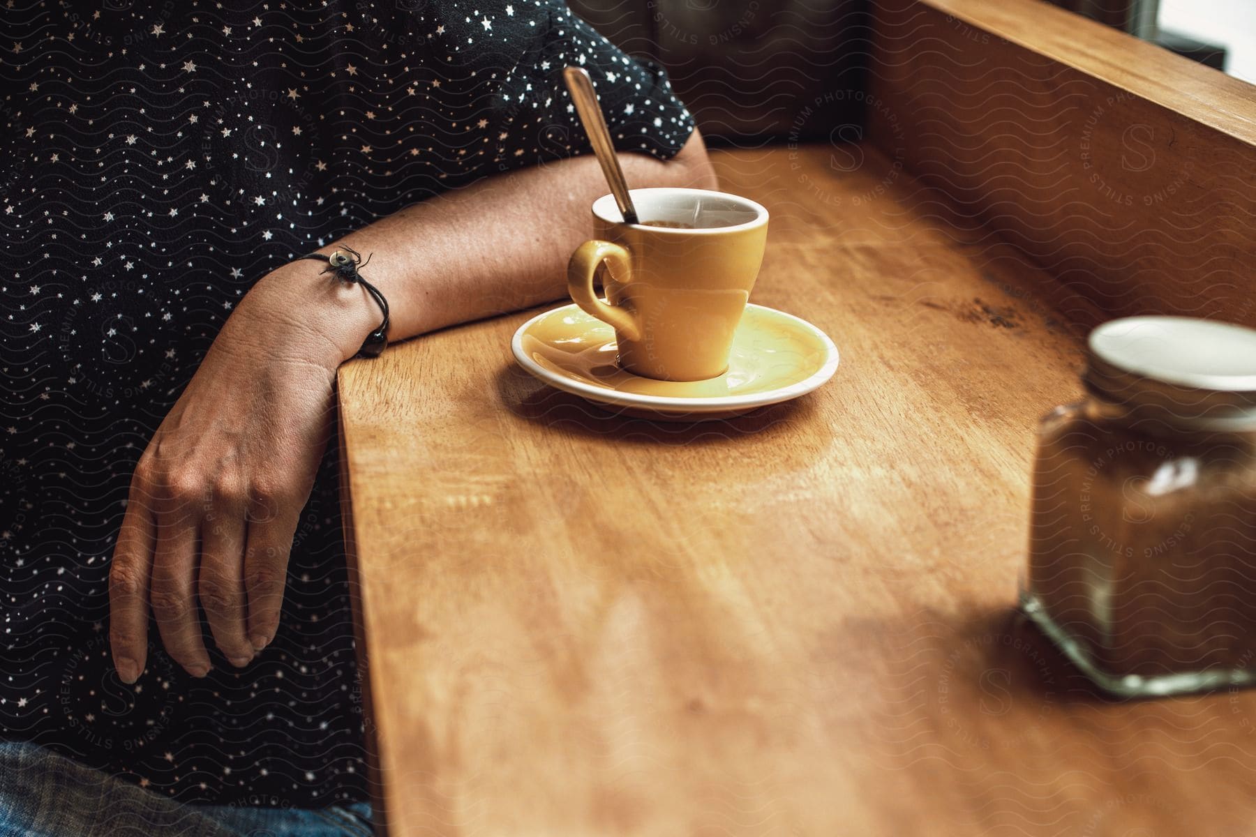 Person leans against wooden counter near window with coffee cup in front of them