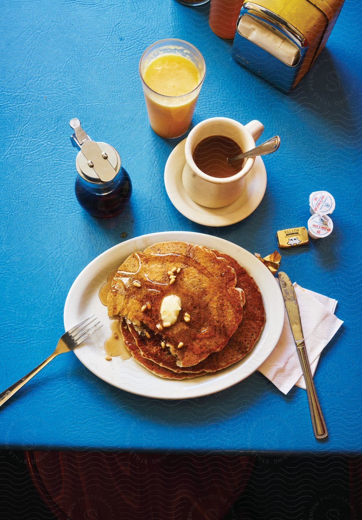 Close up of pancakes on a plate with coffee and a glass of orange juice on a blue table