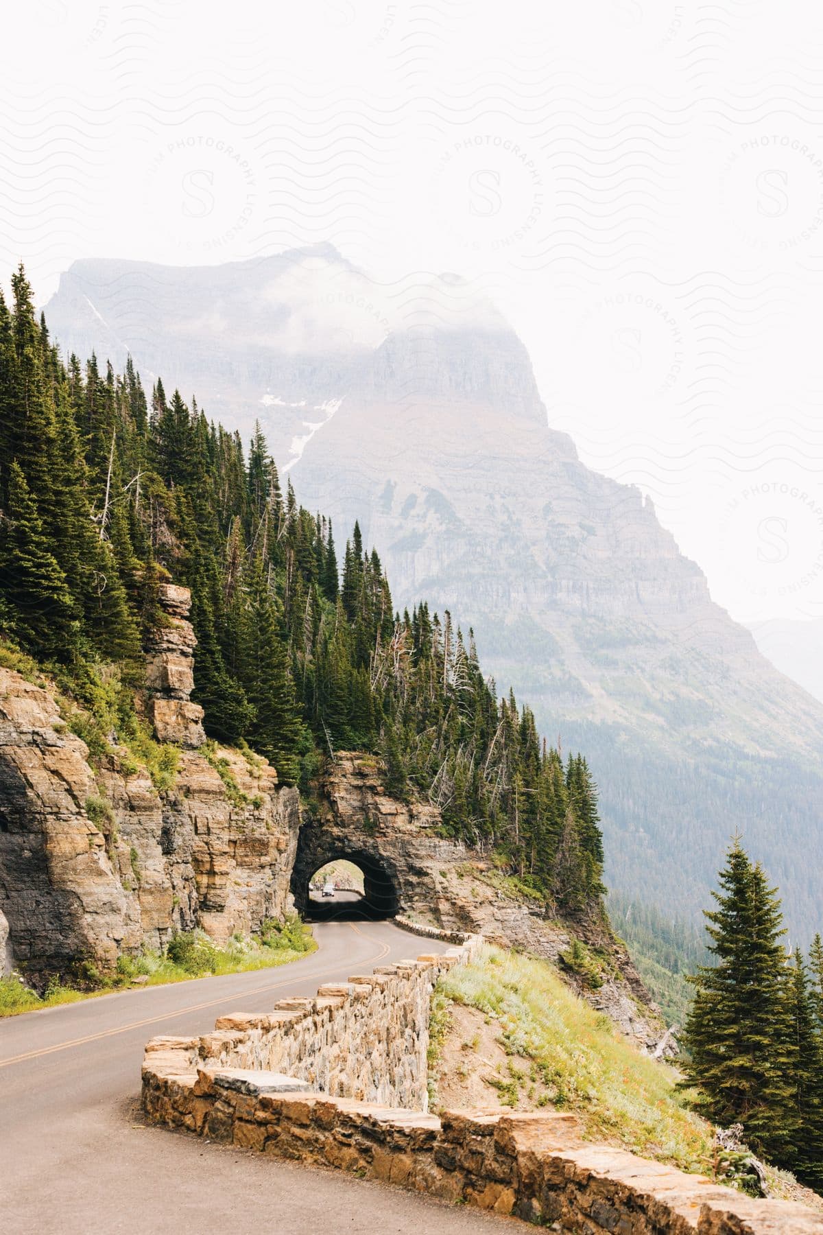 Traffic moves on a forest mountain road with a tunnel through a rock formation