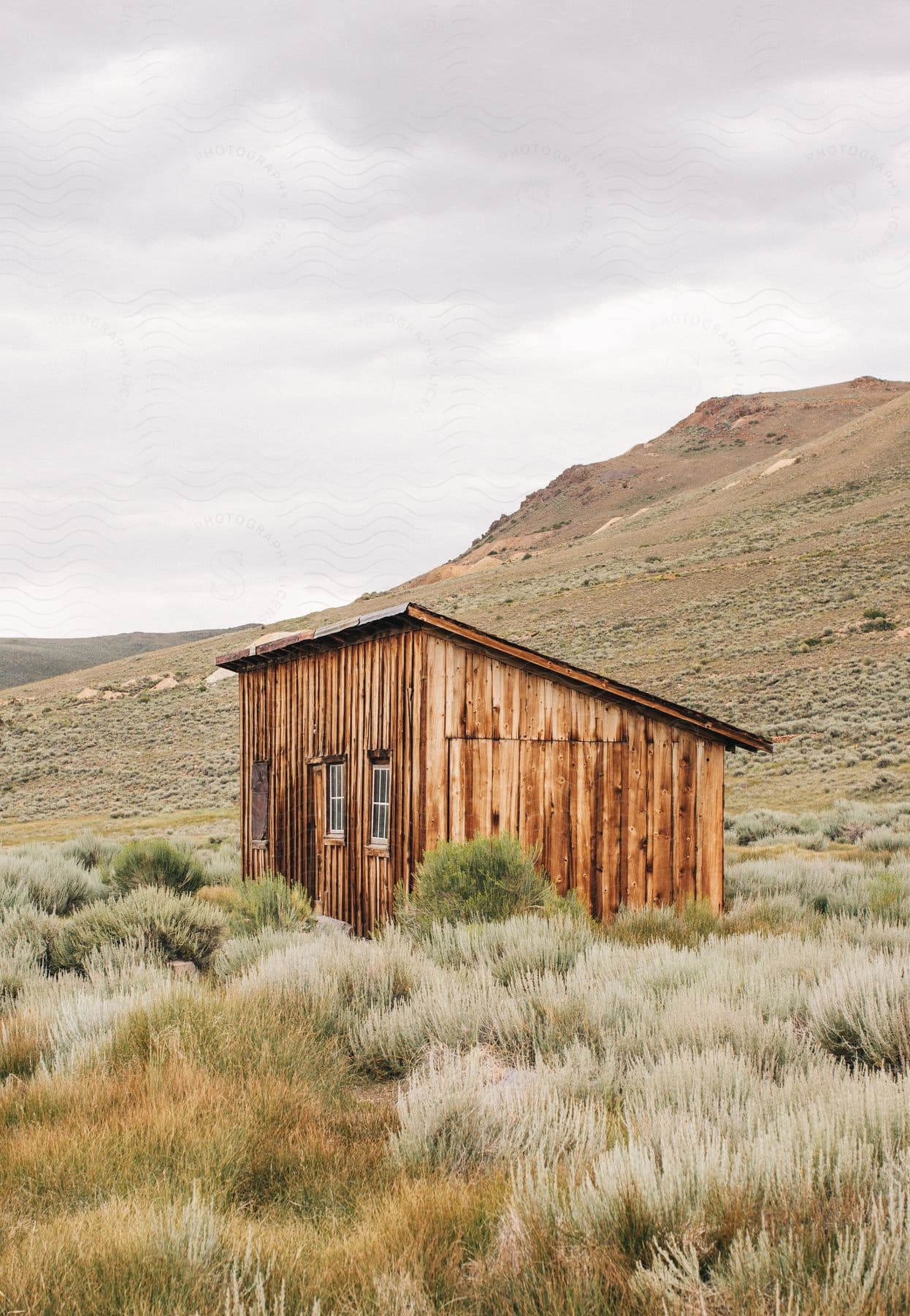 A wooden hut in a landscape with grass and mountains