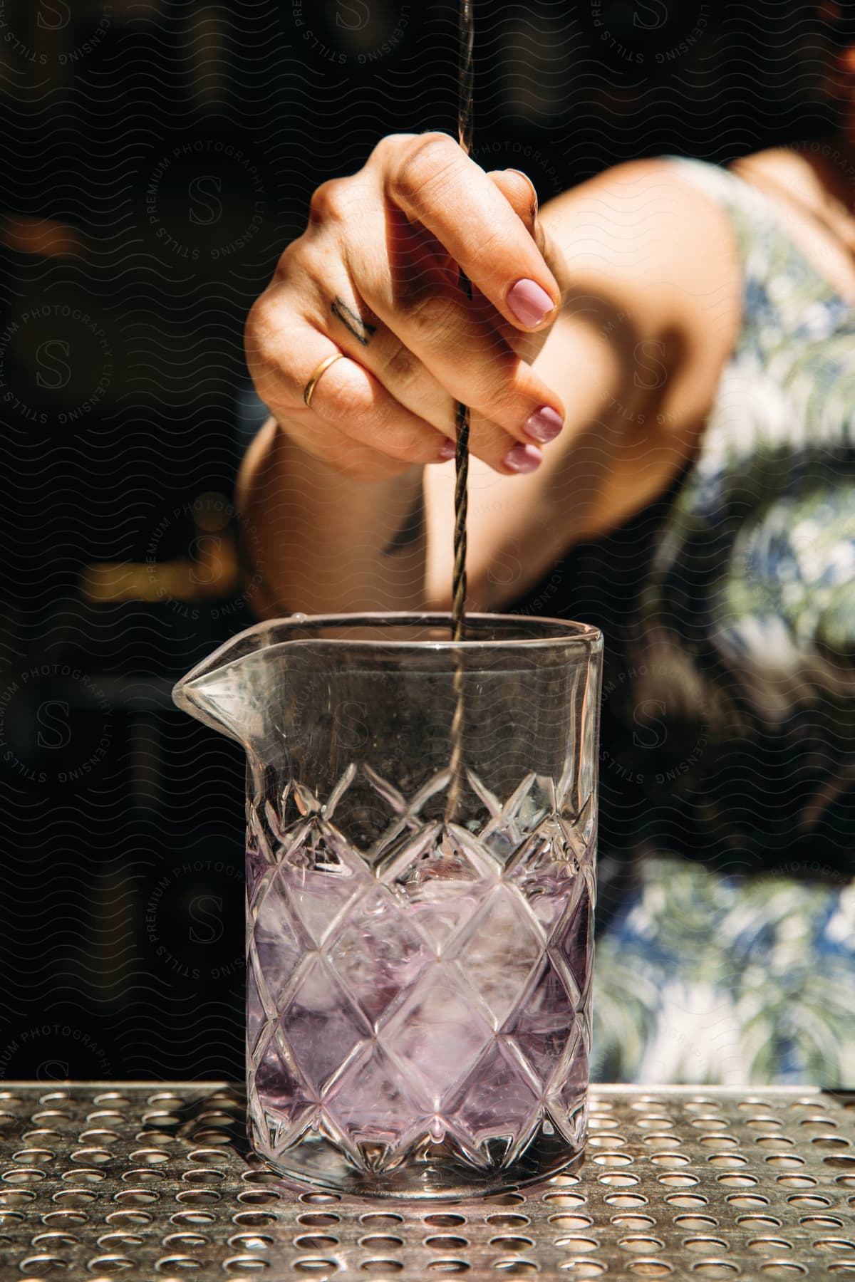 A woman with a tattooed finger stirs a drink in a beaker with a swizzle stick