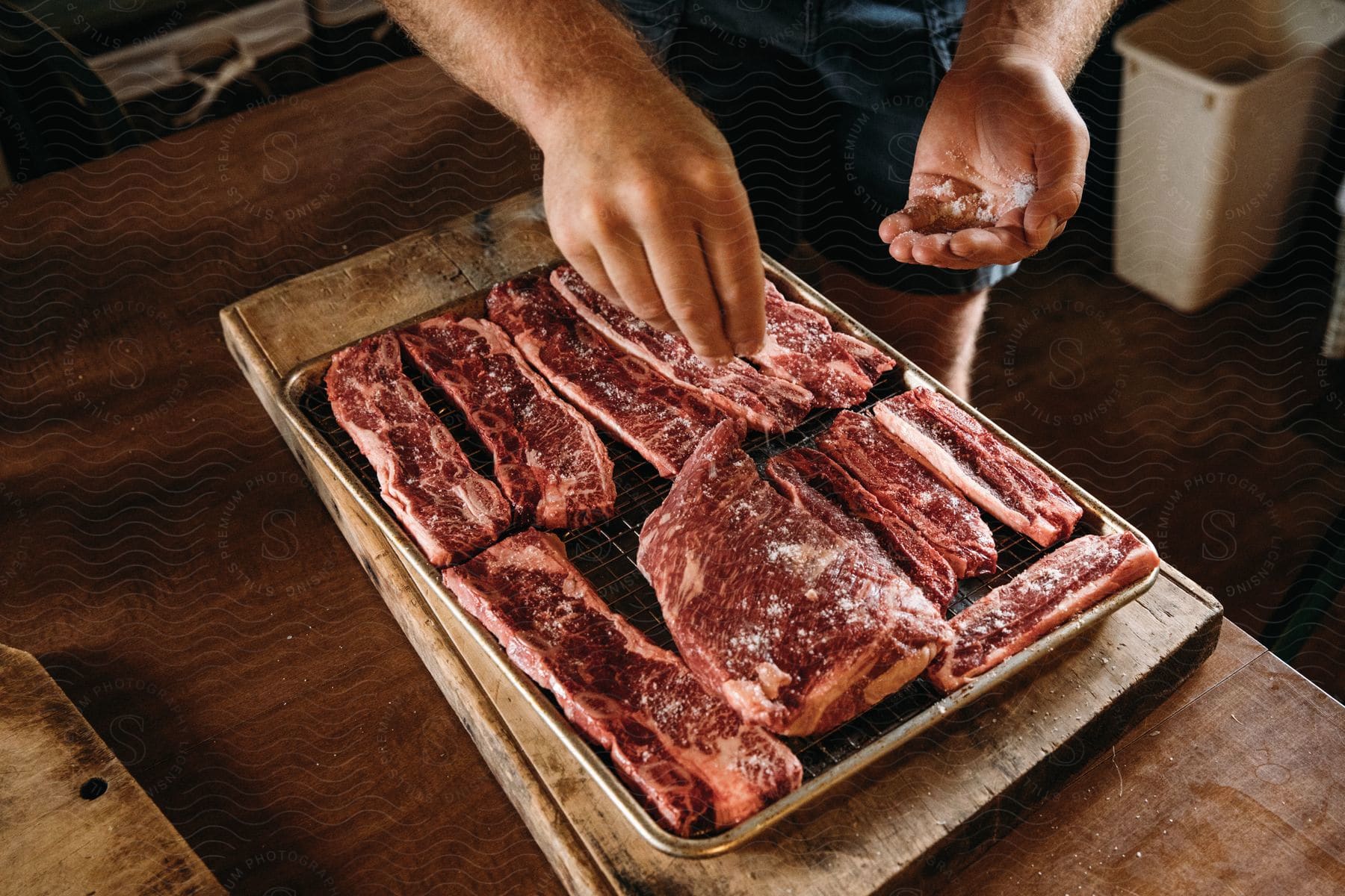 Stock photo of a man salts a tray of short ribs in a kitchen