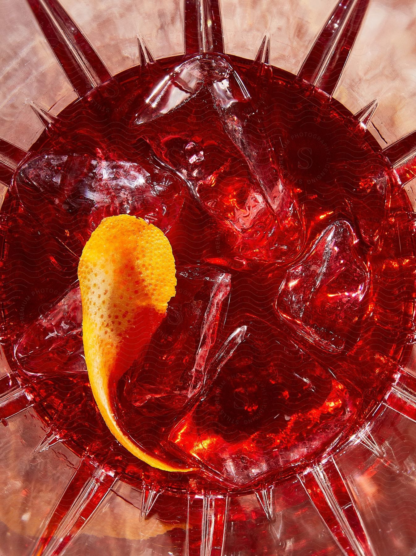 A glass of red drink with orange peel and ice