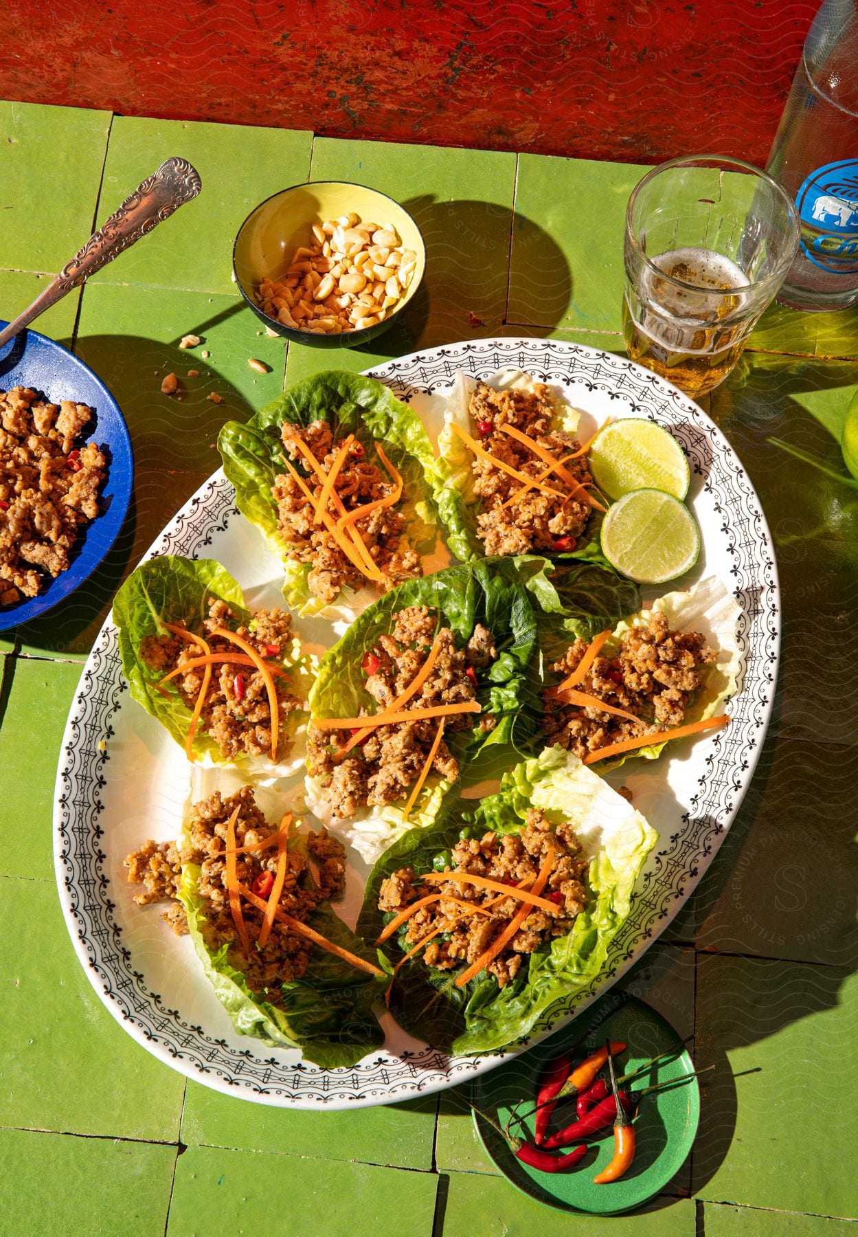 Plate with lemon slices lettuce leaves filled with ground meat and shredded carrot chilies beer and a bowl of corn kernels