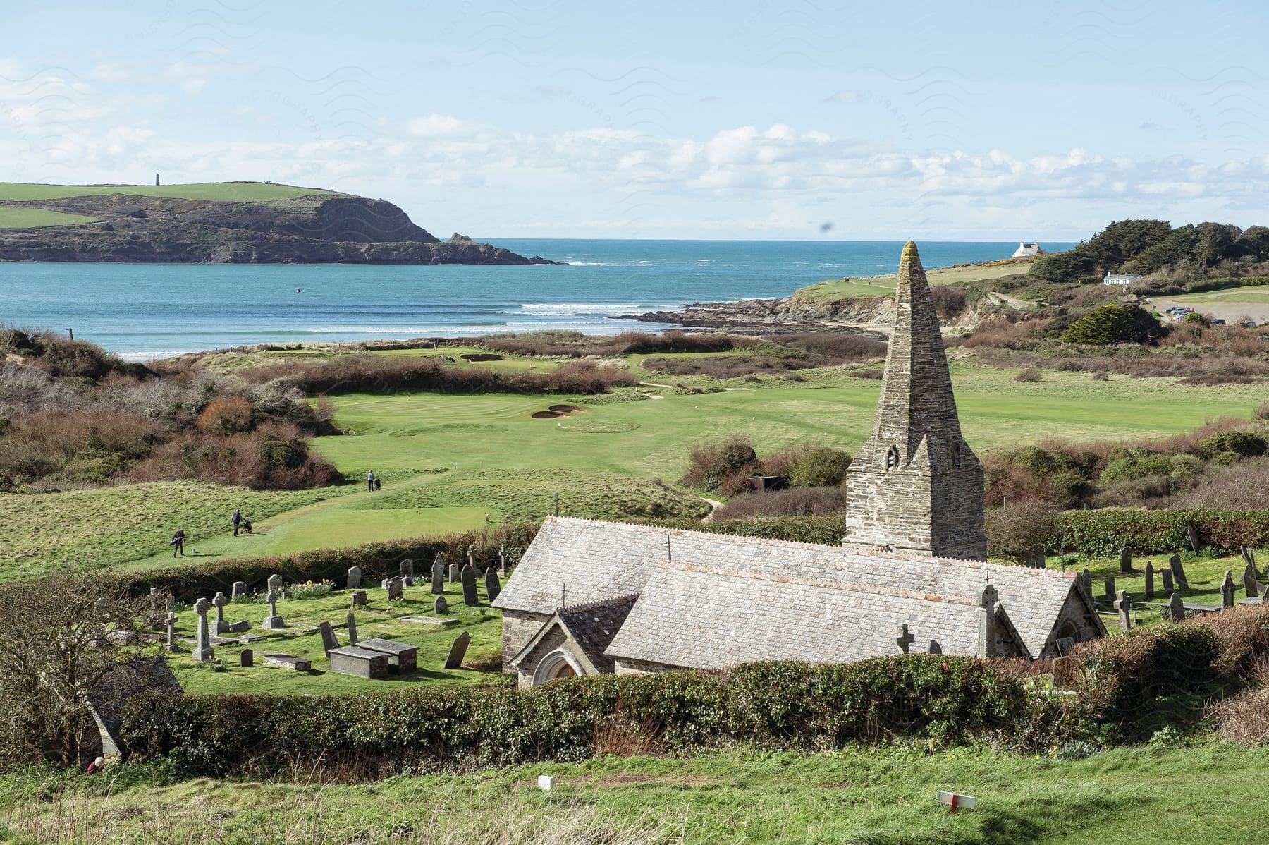 An ancient stone church and graveyard next to a golf course on the coast